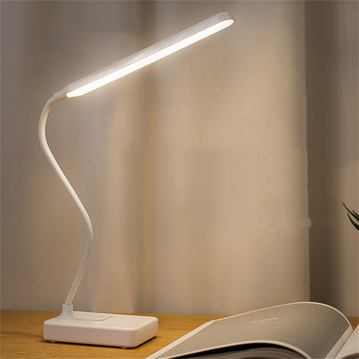 Weiße Schreibtischlampe mit gebogenem Arm, beleuchtet auf einem Schreibtisch.