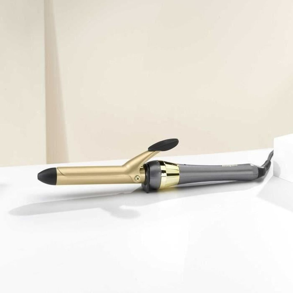 Gold and gray curling iron on a white surface, side view.