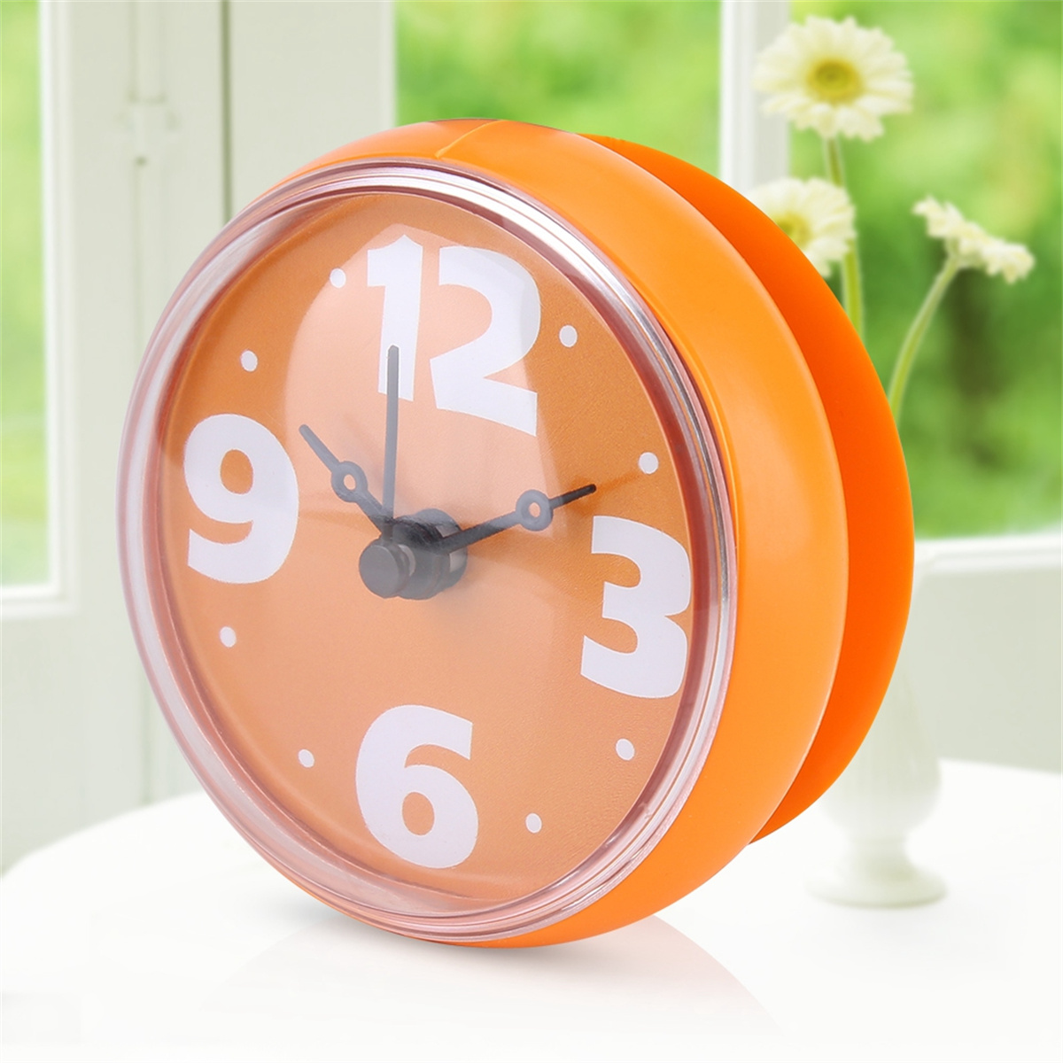 Orangener Wecker, rundes Zifferblatt mit weißen Zahlen und ein weißer Tisch mit Vase.