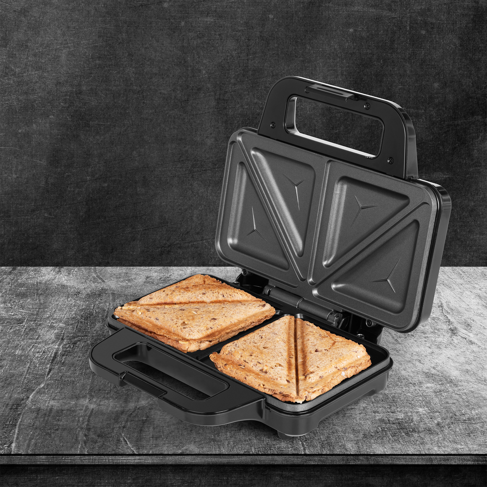 Ein schwarzer Sandwichmaker mit zwei Sandwiches. Die Sandwiches sind in Dreiecke geschnitten.