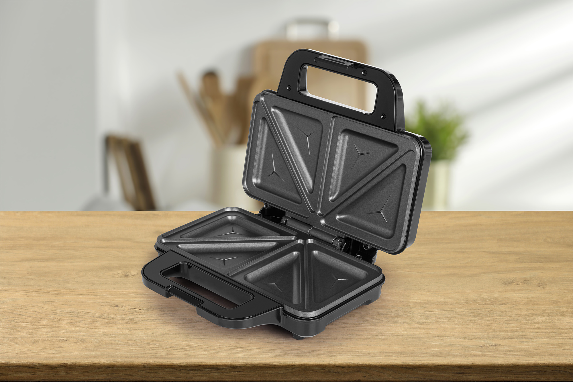 Schwarzer Sandwichmaker offen auf einem Holztisch, Küchenhintergrund.