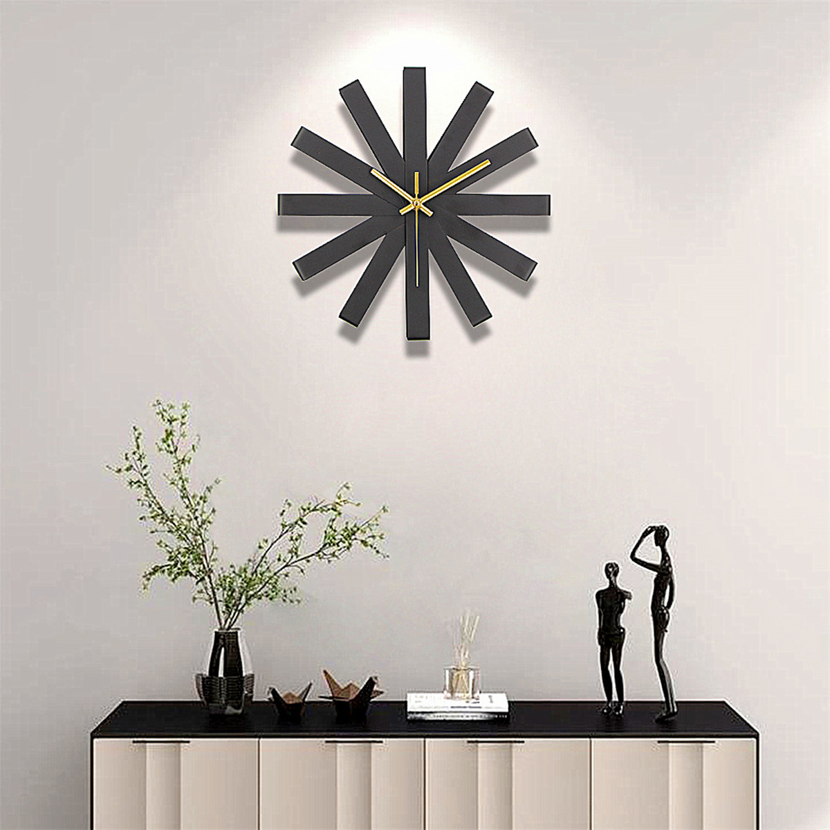 Moderne schwarze Uhr mit gelben Zeigern an einer weißen Wand. Darunter ein schwarzer Tisch mit Deko.