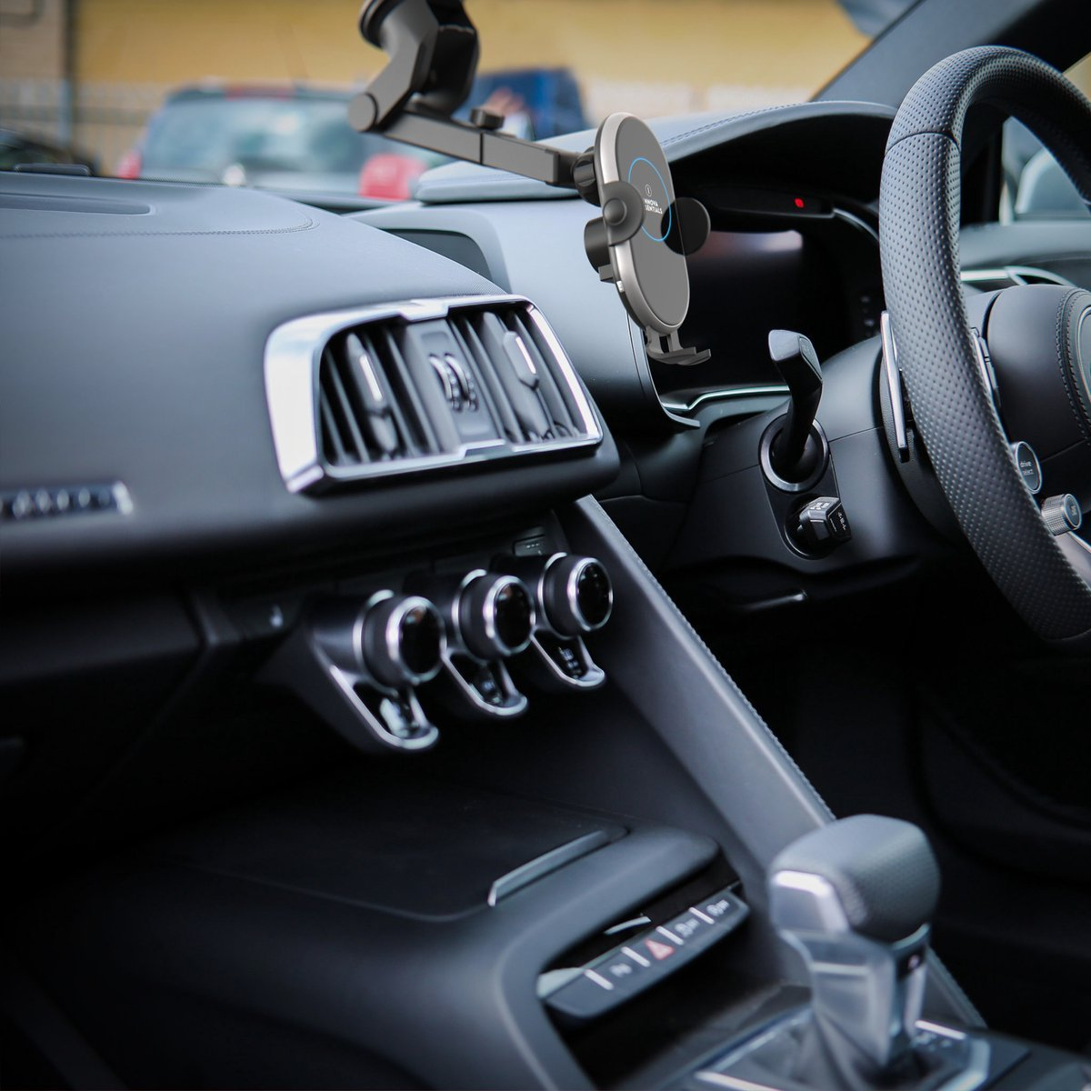 Ein Autointerieur mit einem Telefonhalter am Armaturenbrett. Telefon im Halter. Lenkrad sichtbar.
