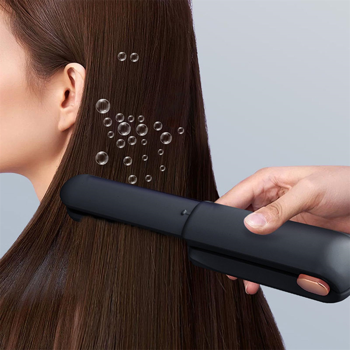 Hand einer Frau, die einen Haarglätter auf braunem Haar benutzt. Blasen schweben herum.