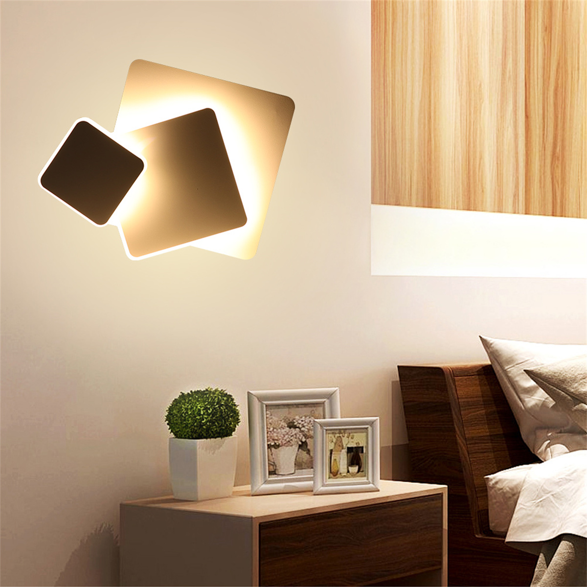 Moderne Wandlampe mit Pflanze, Rahmen und Nachttisch aus Holz in einem Raum.