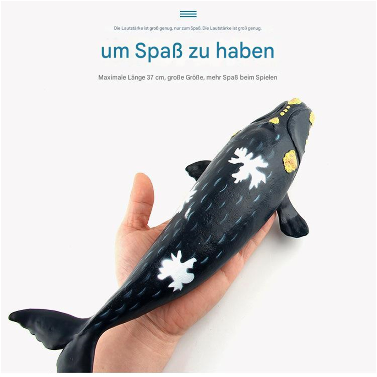Ein schwarzer Spielzeugwal mit weißen Markierungen, gehalten in einer Hand, auf weißem Hintergrund.