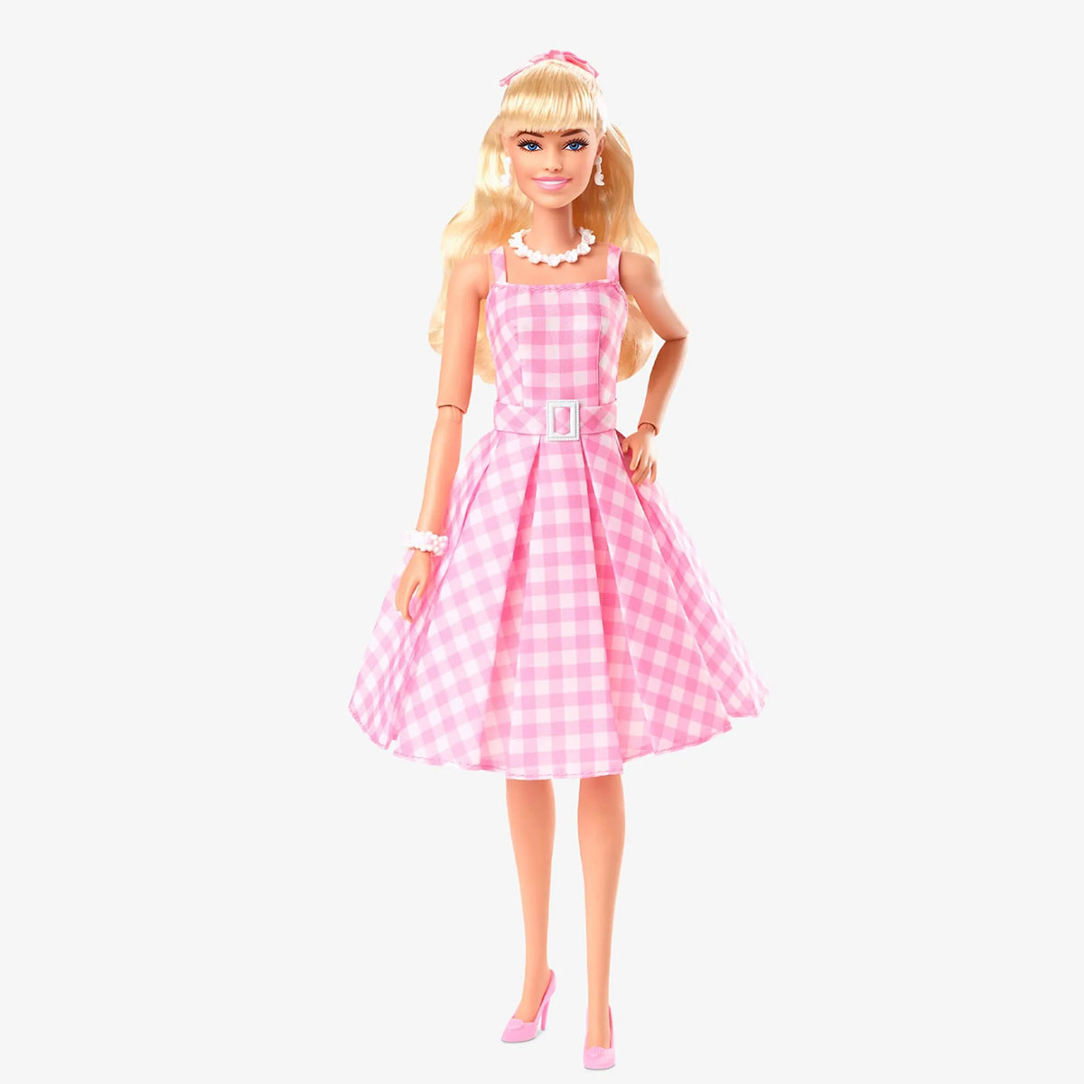 Lalka Barbie w różowo-białej sukience w kratkę i różowych butach, stojąca na białym tle.
