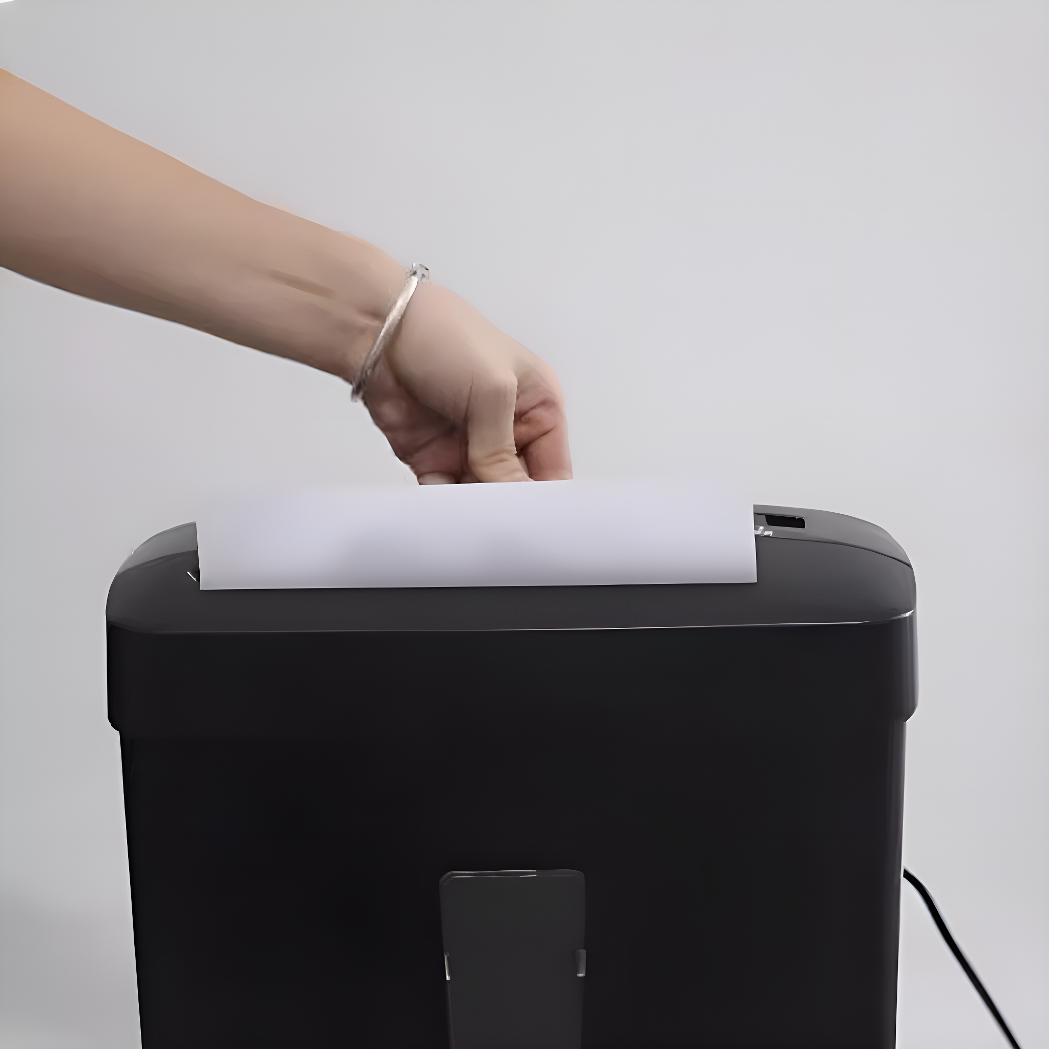 Eine Hand legt weißes Papier in einen schwarzen Aktenvernichter auf weißem Hintergrund.