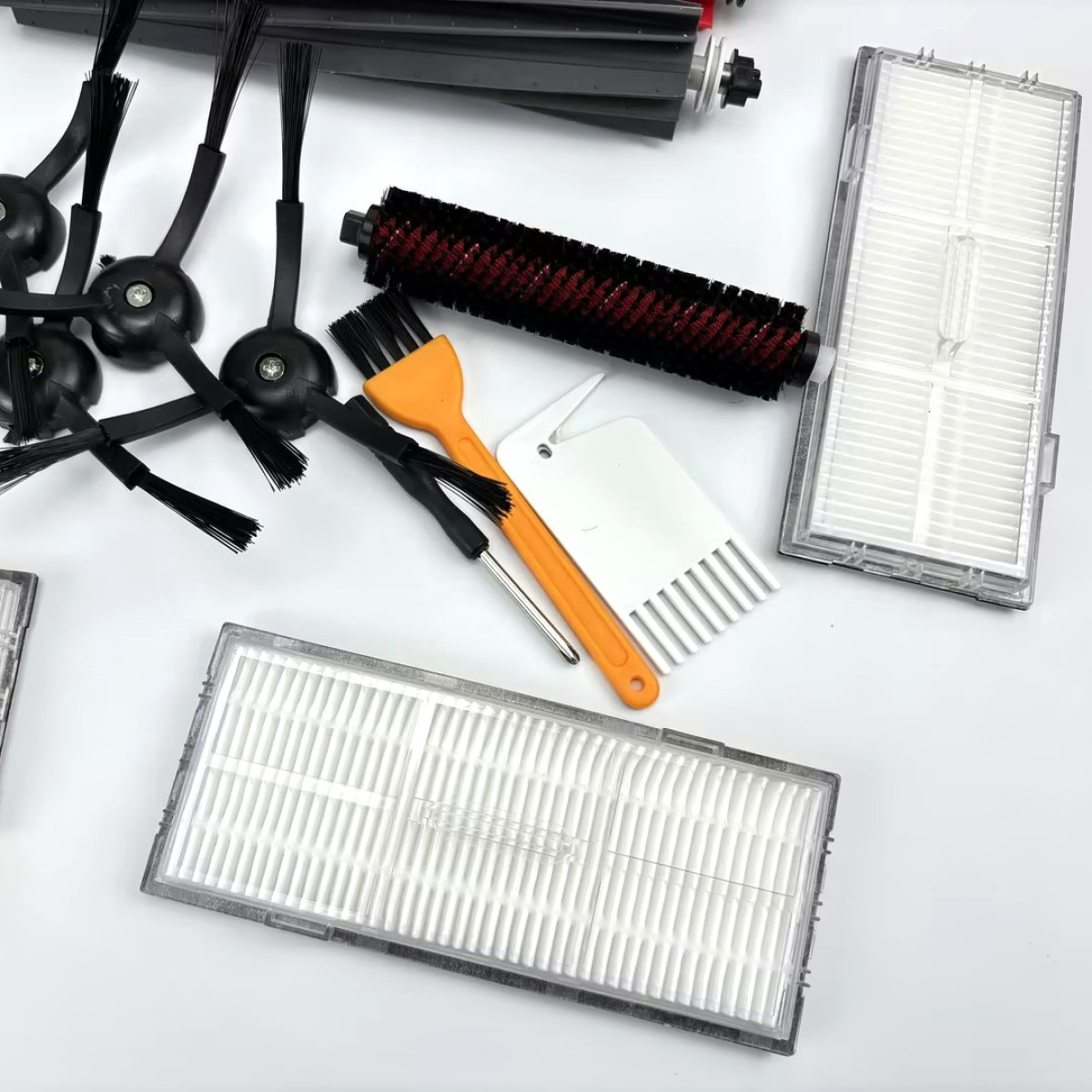 Różne akcesoria do czyszczenia i filtry do robota odkurzającego, ułożone na białej powierzchni.