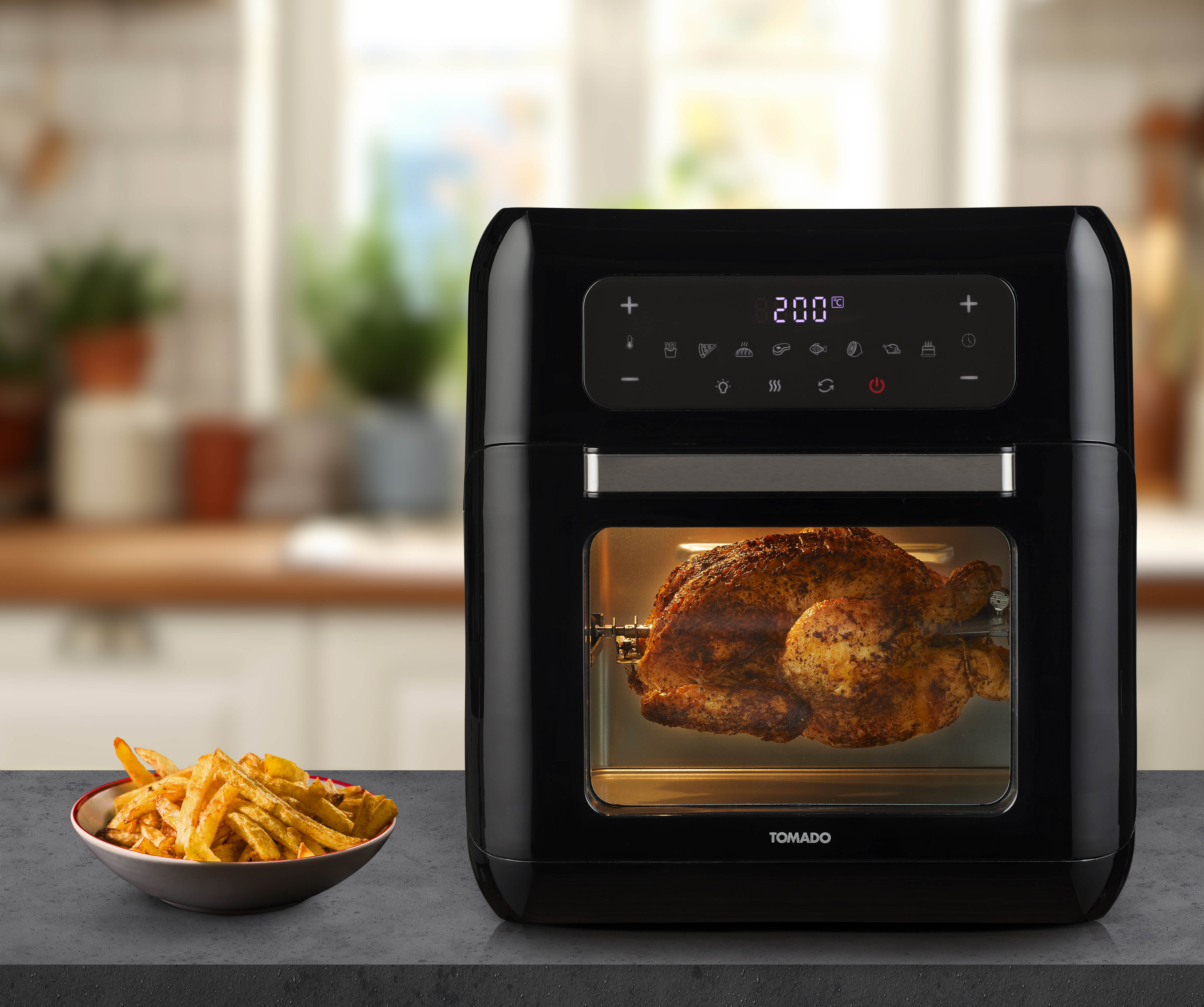 Black air fryer with a cooked chicken inside, and fries on a plate.