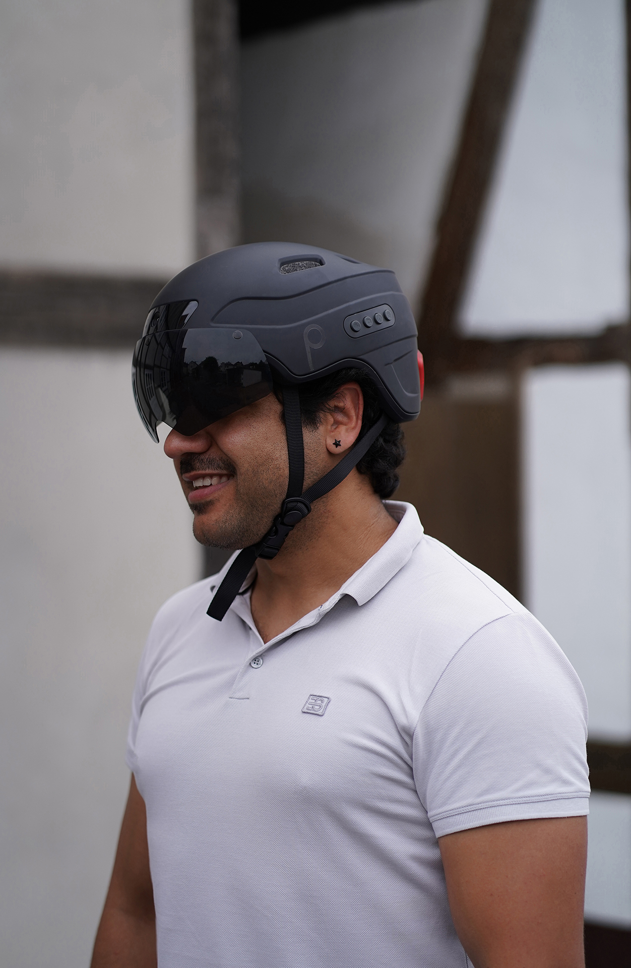 Mann trägt einen schwarzen Fahrradhelm mit Visier und lächelt. Der Helm hat Licht- und Kopfhörerfunktionen.