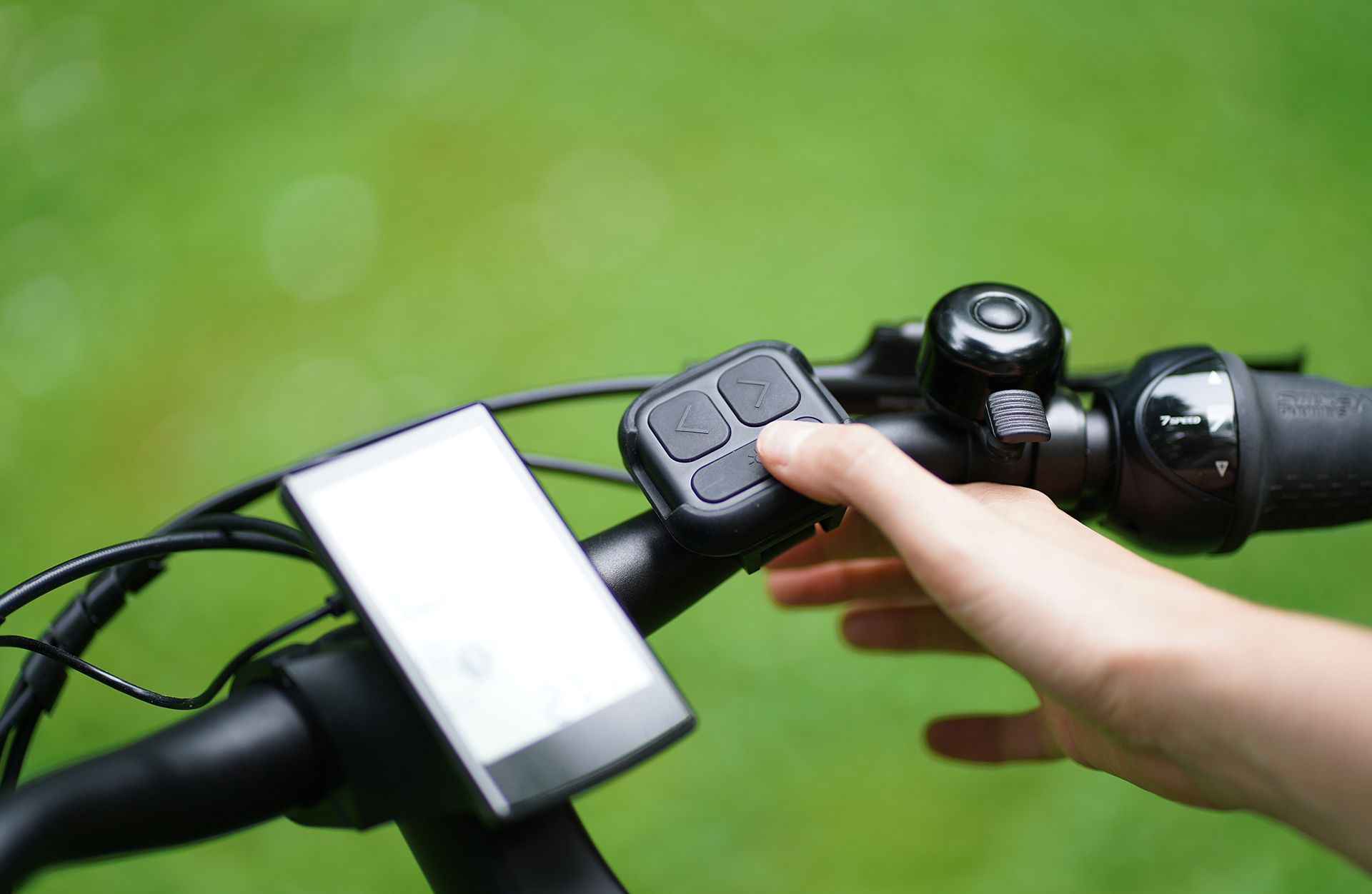 Eine Hand drückt eine Taste an einem Fahrradlenker. Ein Display und eine Klingel sind sichtbar.