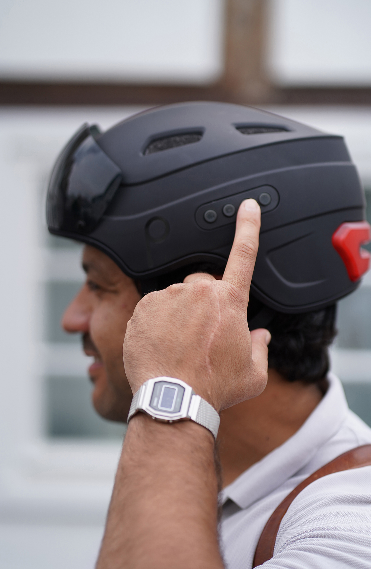 Ein Mann mit schwarzem Helm mit Visier, der die Knöpfe berührt. Er trägt eine Uhr.