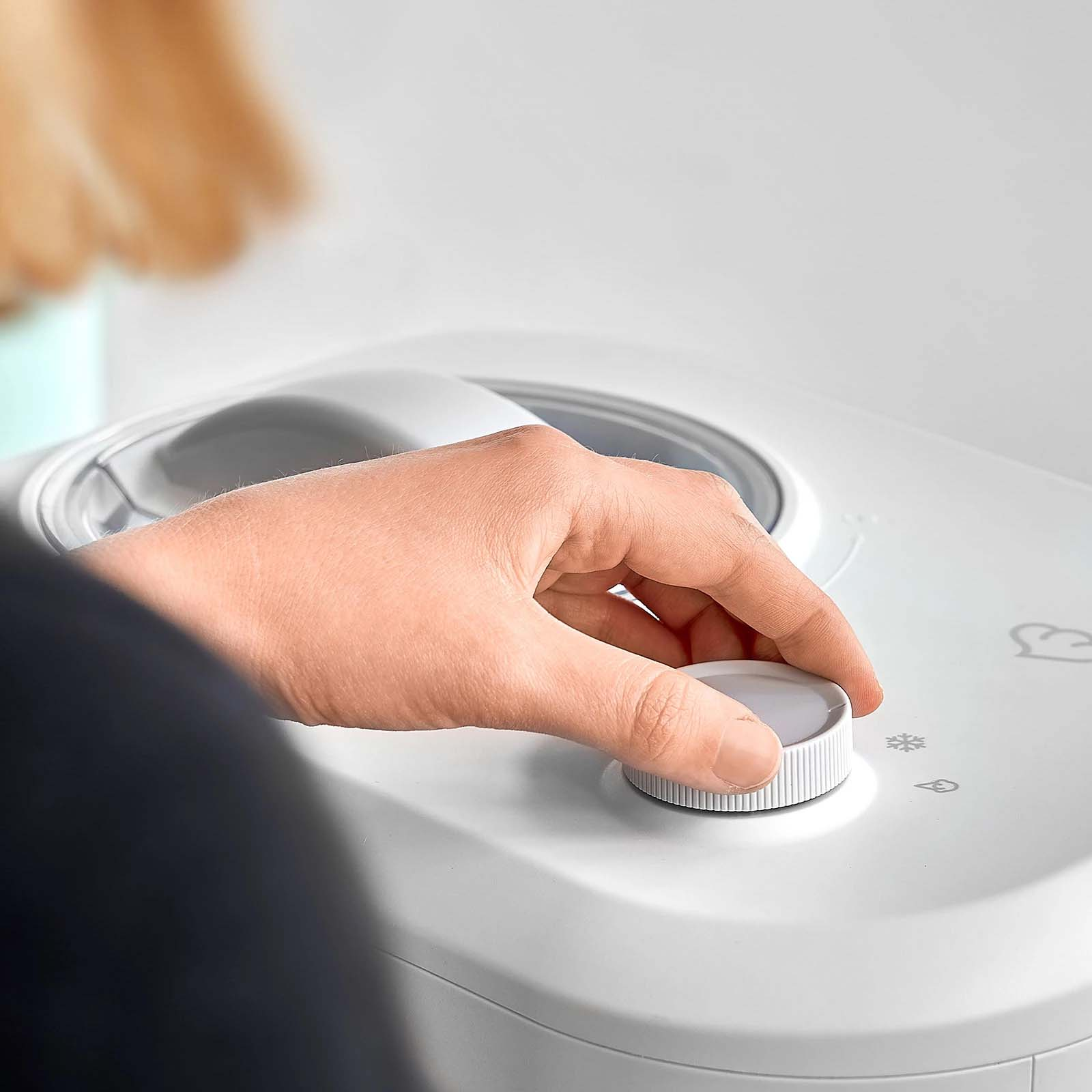 Eine Hand dreht einen weißen Drehregler an einem weißen Gerät, möglicherweise einer Maschine.