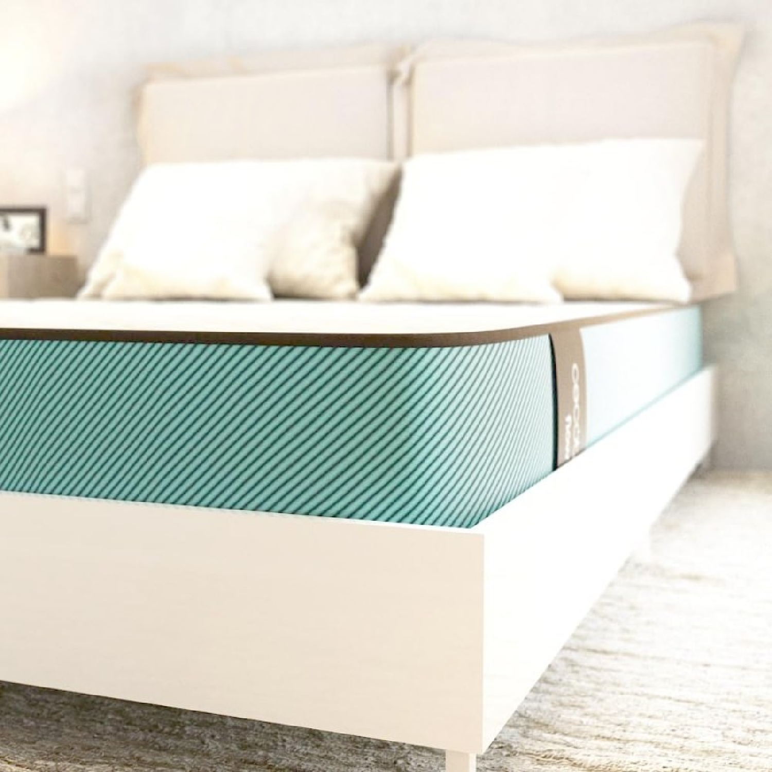 Una cama con un colchón verde azulado, almohadas blancas y una cabecera beige claro.