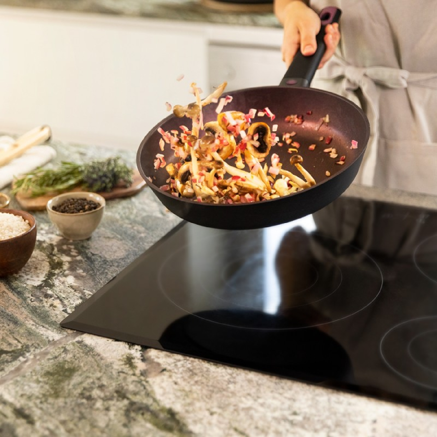 Una persona sta saltando il cibo in una padella. Vengono gettati funghi e cipolle. Sono visibili anche altri ingredienti e un fornello.