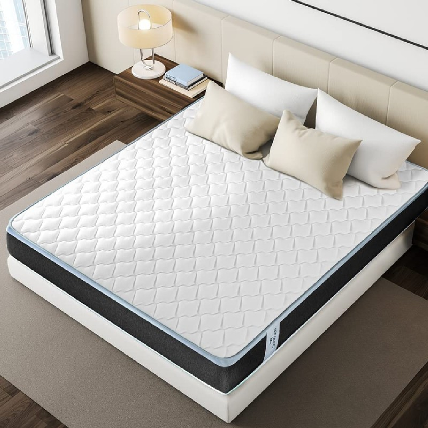 Un colchón blanco sobre una cama plataforma, con almohadas y una lámpara. Habitación de tonos neutros, de día.