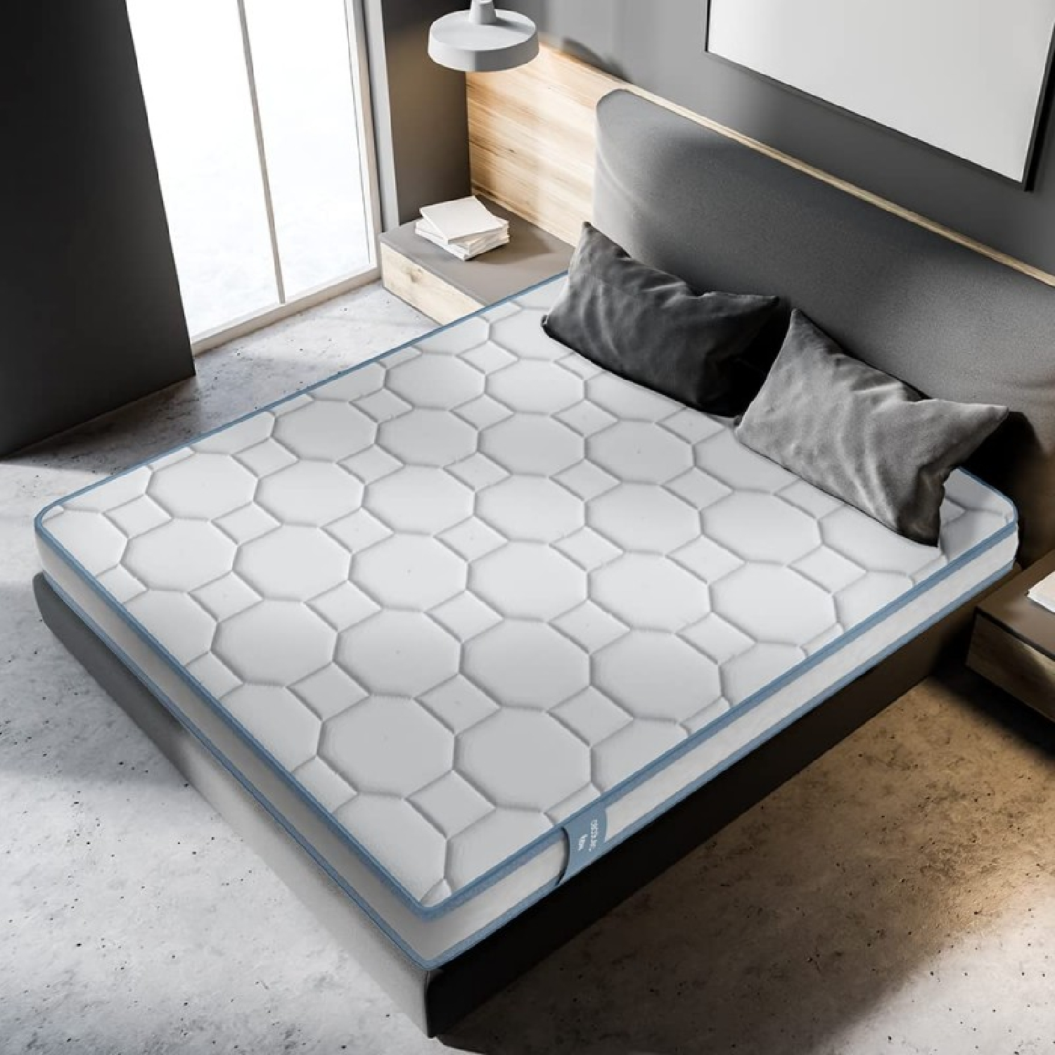 Una cama con colchón blanco, almohadas y cabecero gris, en un entorno de habitación.