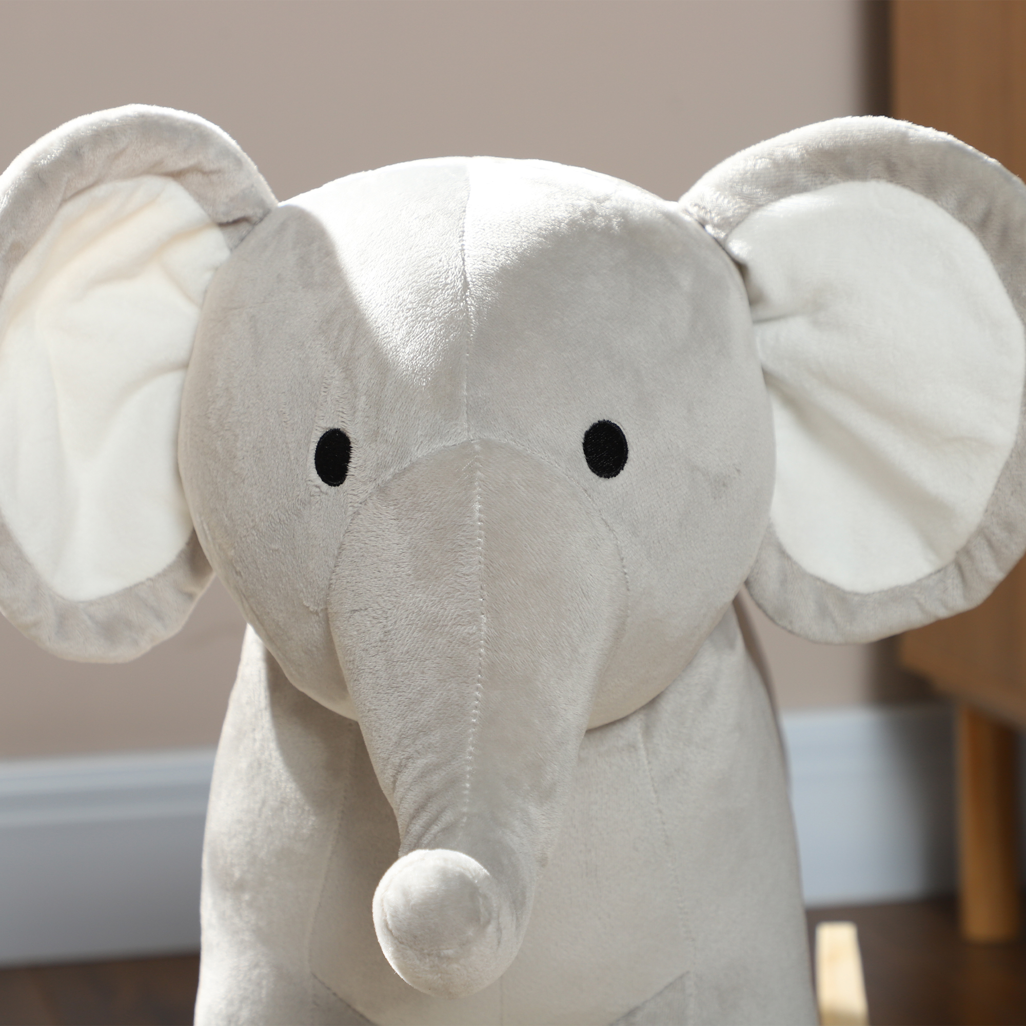 Peluche a forma di elefante grigio. Grandi orecchie e occhi neri. Sfondo chiaro.