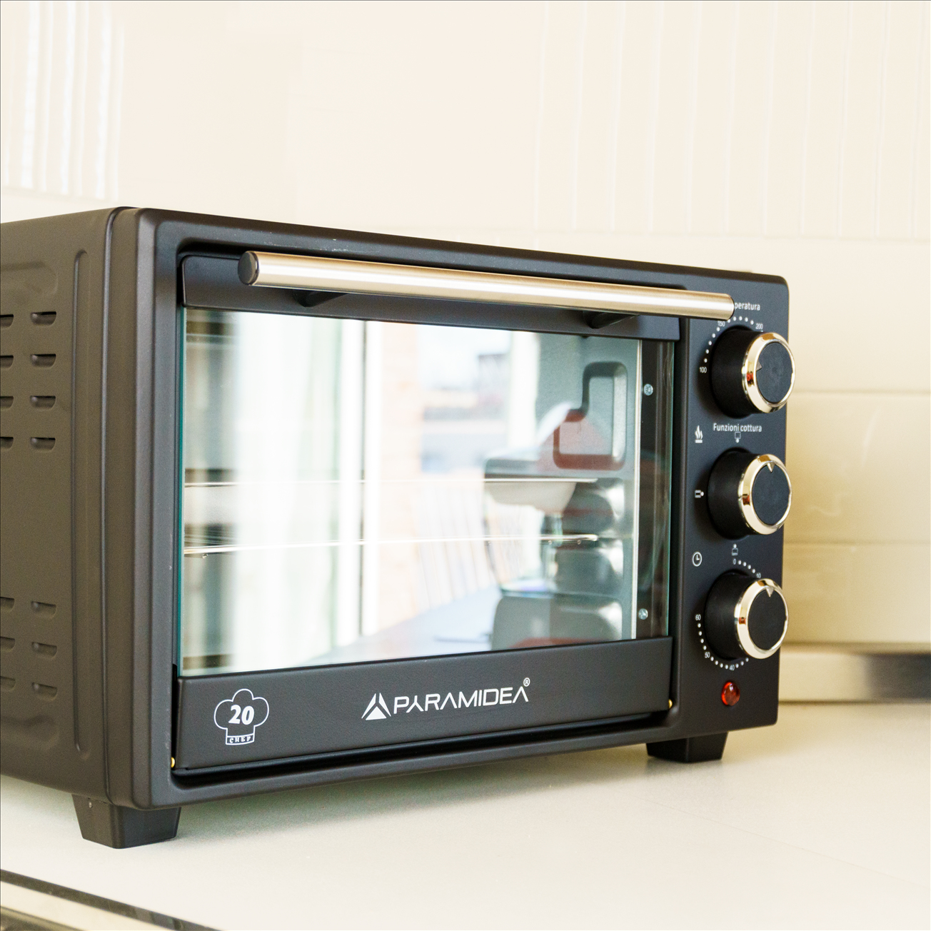 Un forno da banco nero con tre manopole di controllo e una porta a vetro, su sfondo bianco.