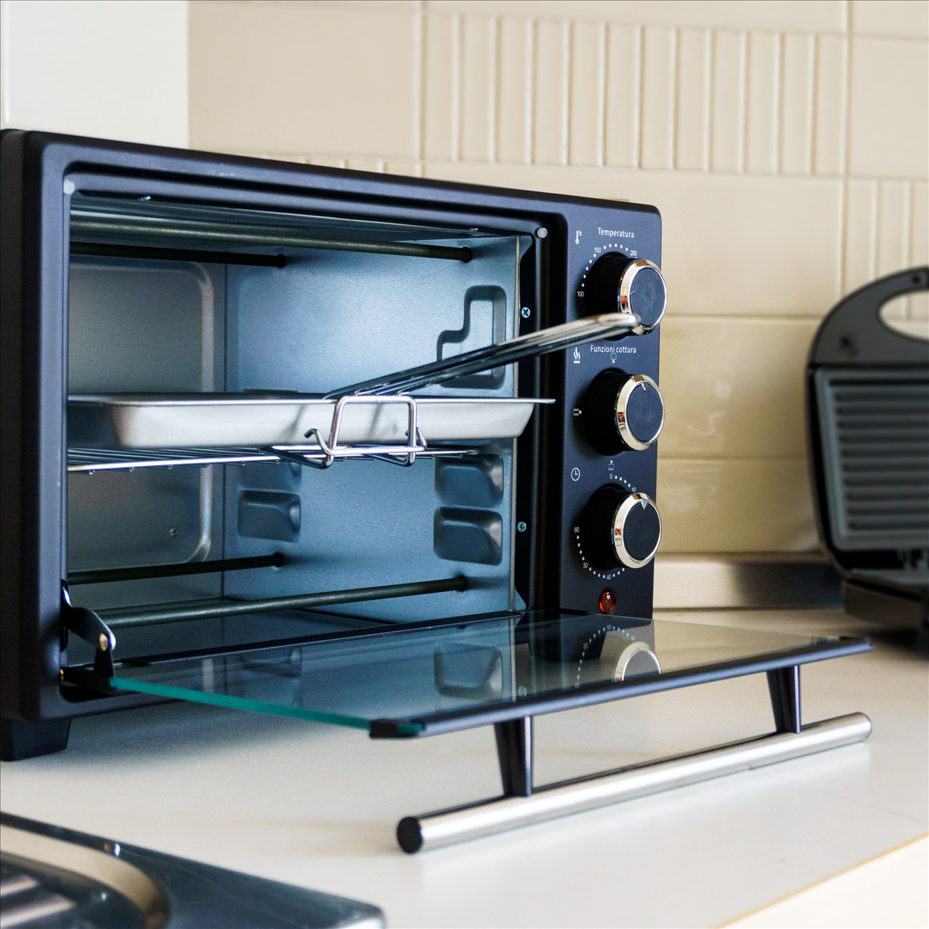 Un forno nero con porta a vetro e teglia all'interno, su una superficie bianca.