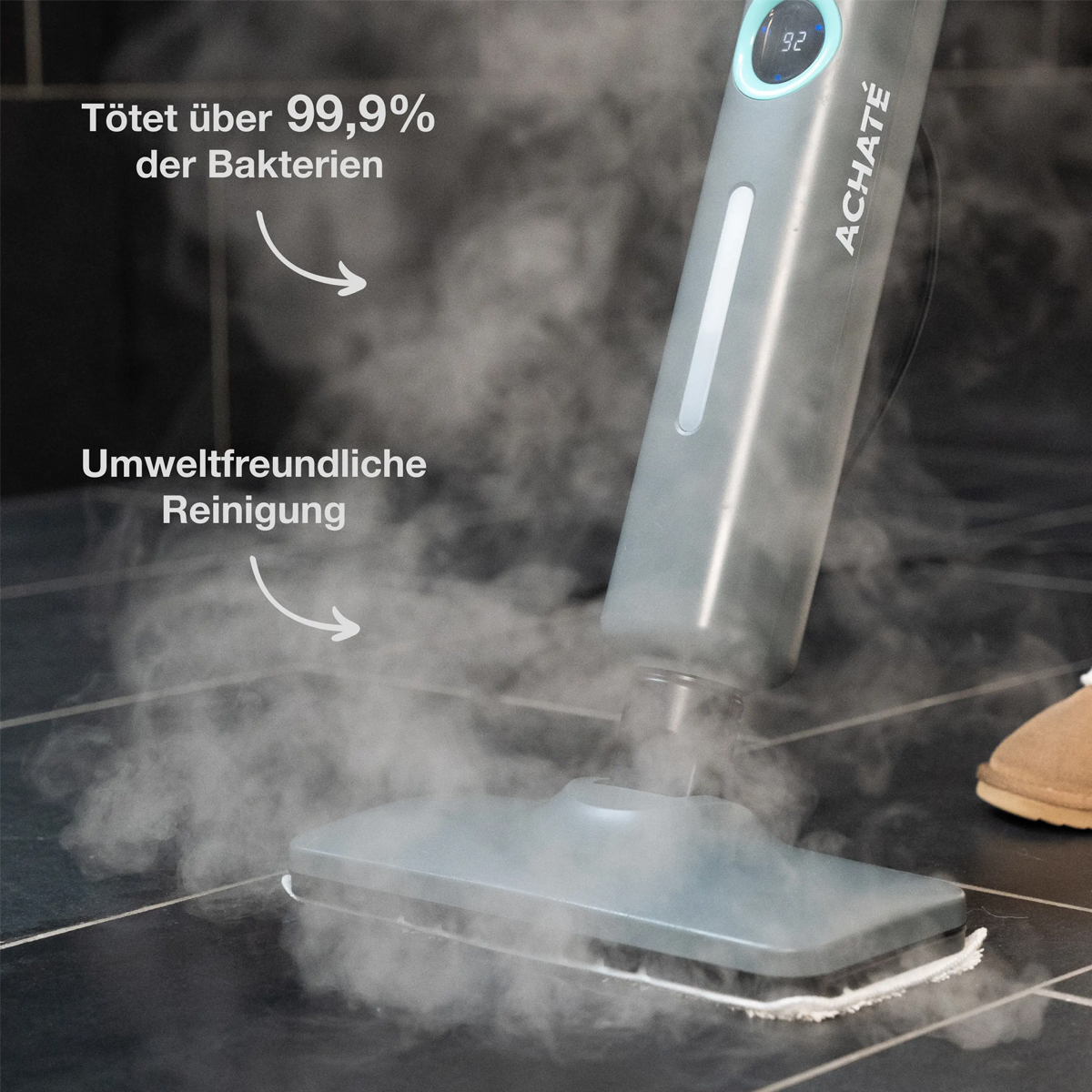 Ein Dampfreiniger reinigt schwarze Fliesen. Dampf steigt auf. Text: tötet Bakterien.