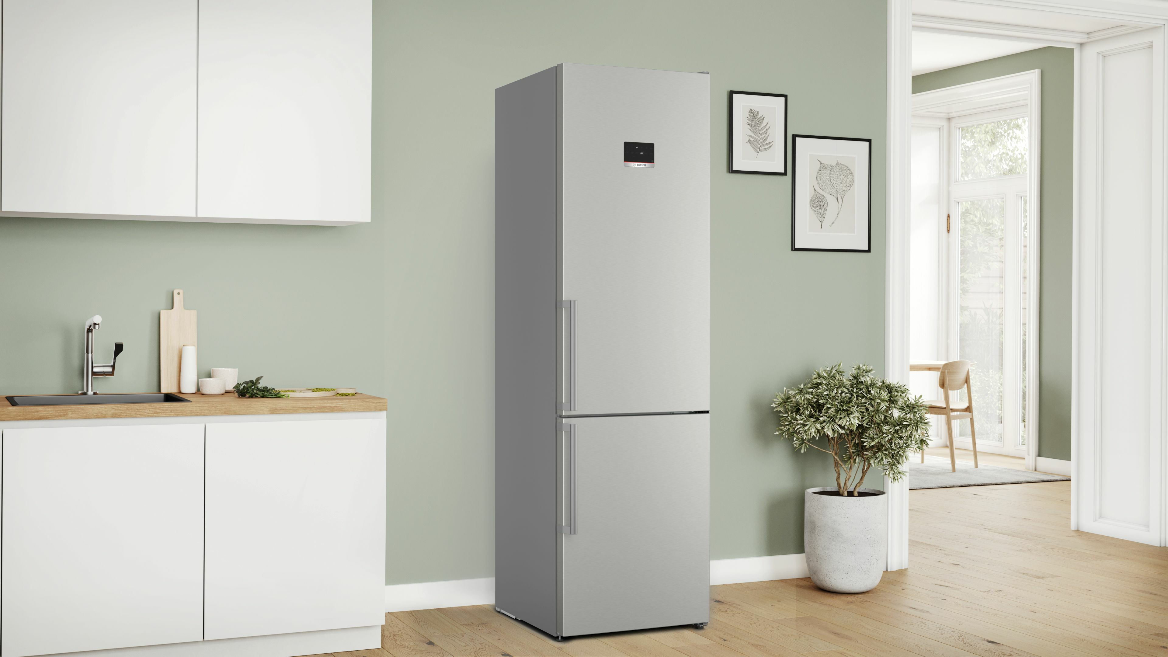 Refrigerador plateado en una cocina con gabinetes blancos y pared verde claro.