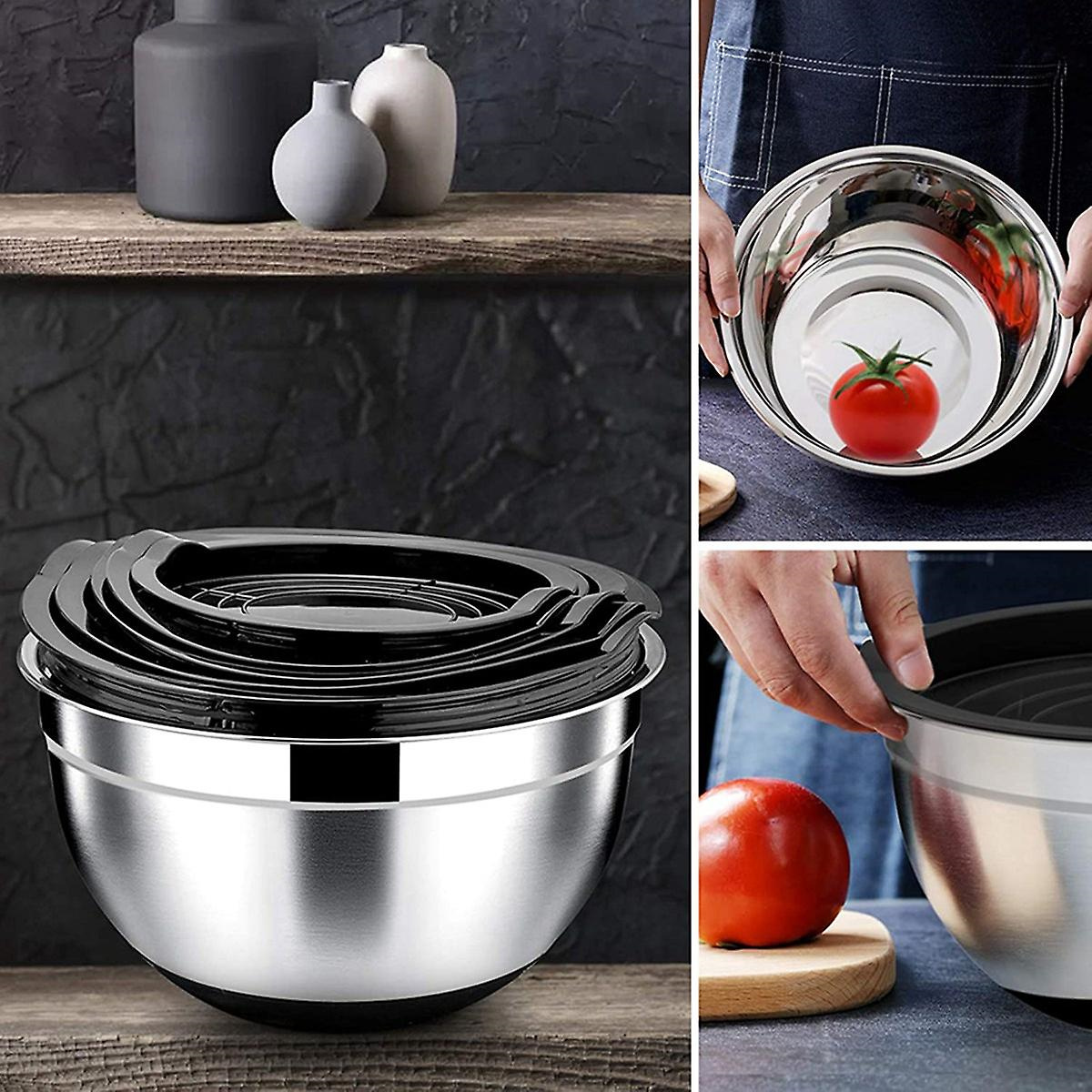 Edelstahl-Rührschüsseln mit Deckeln. Eine Tomate liegt in einer Schüssel. Andere Schüsseln und Gegenstände sichtbar.