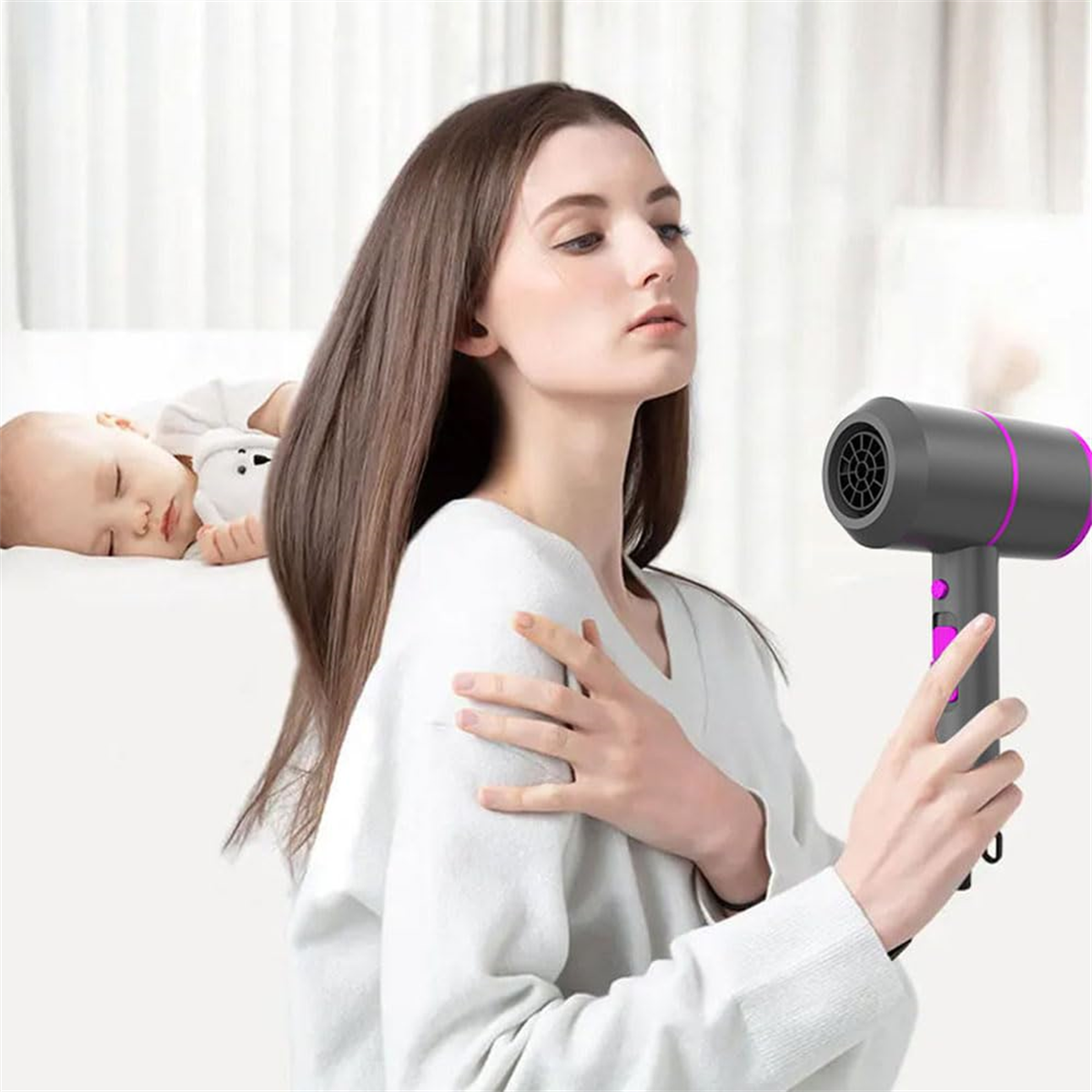 Eine Frau hält einen Haartrockner, im Hintergrund schläft ein Baby auf einer weißen Oberfläche.