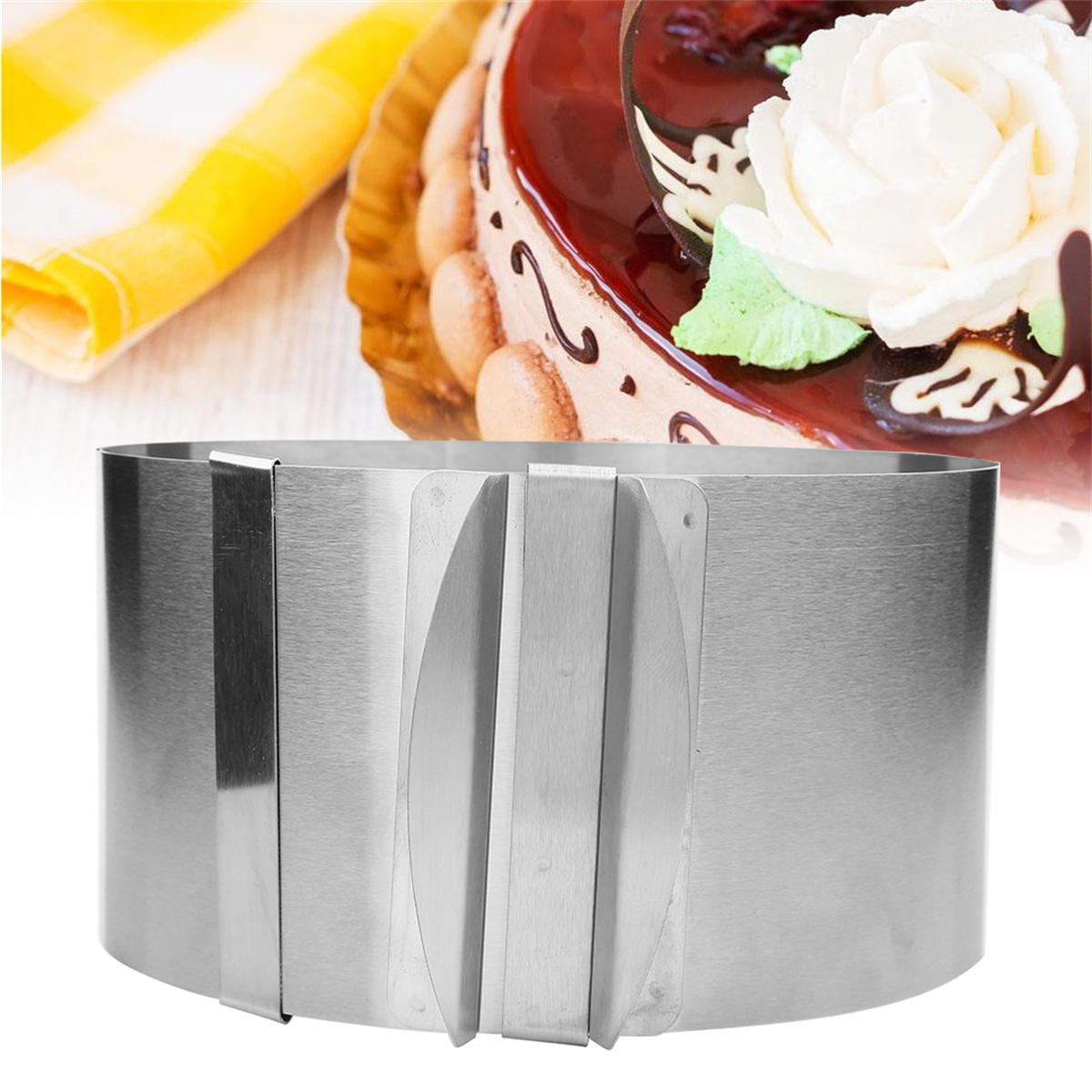 Metall-Kuchenring mit einem Kuchen im Hintergrund. Der Kuchen hat eine weiße Blume und Zuckerguss.