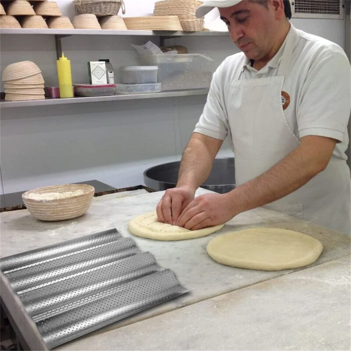 Ein Bäcker macht Pizza. Er drückt Teig auf eine Theke, mit einem gelochten Backblech.