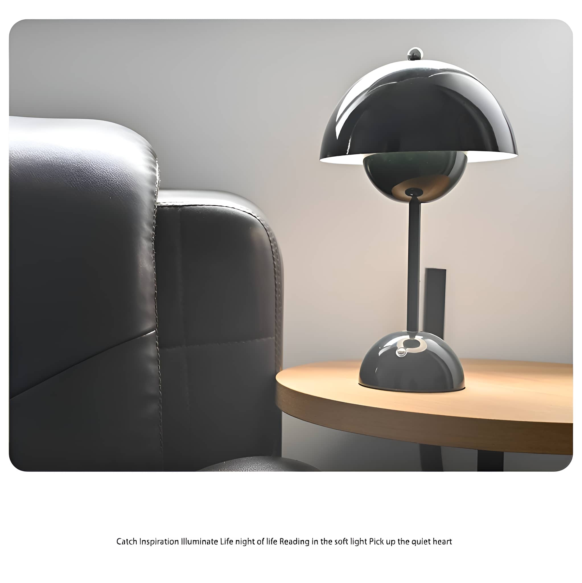 Schwarz-graue Lampe auf einem hölzernen Beistelltisch neben einer schwarzen Ledercouch in einem neutralen Raum.