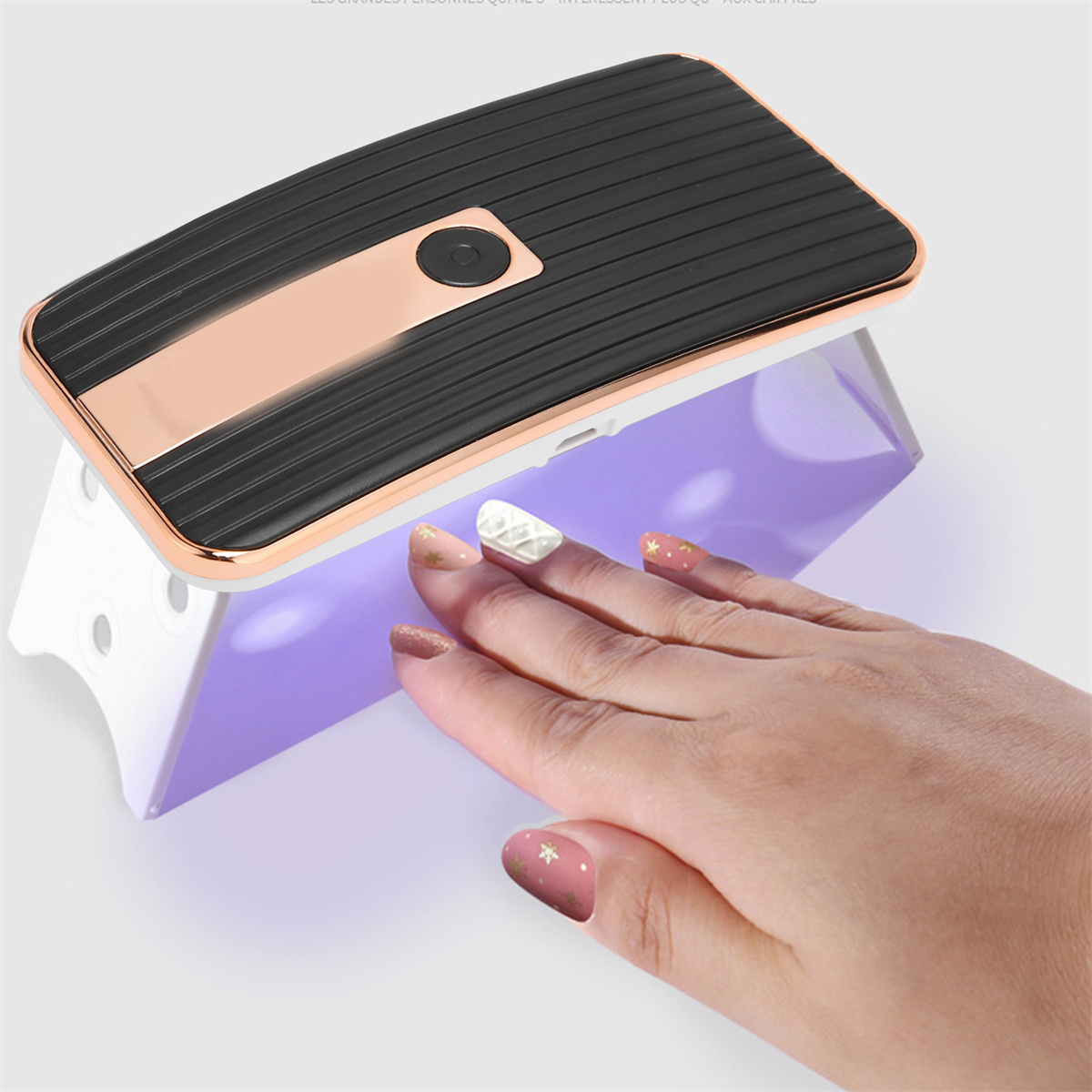 Eine Hand liegt unter einer Nagellampe. Die Nägel sind lackiert und unter der Lampe.