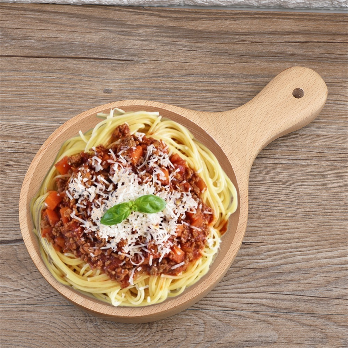 Spaghetti mit Fleischsoße, Käse und Basilikumblatt auf einem Holzbrett mit Griff serviert.