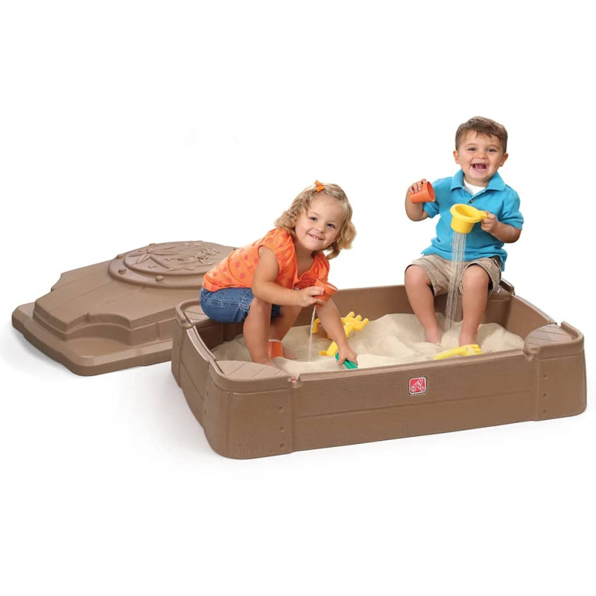 Zwei Kinder spielen in einem Sandkasten. Einer schüttet Sand aus einem gelben Becher. Der andere benutzt eine kleine grüne Schaufel.