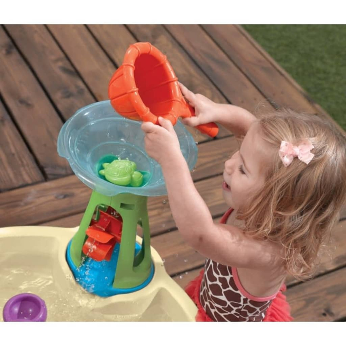 Ein junges Mädchen spielt mit einem Wassertisch und gießt Wasser mit einem orangefarbenen Schöpfer in ein blaues Becken.