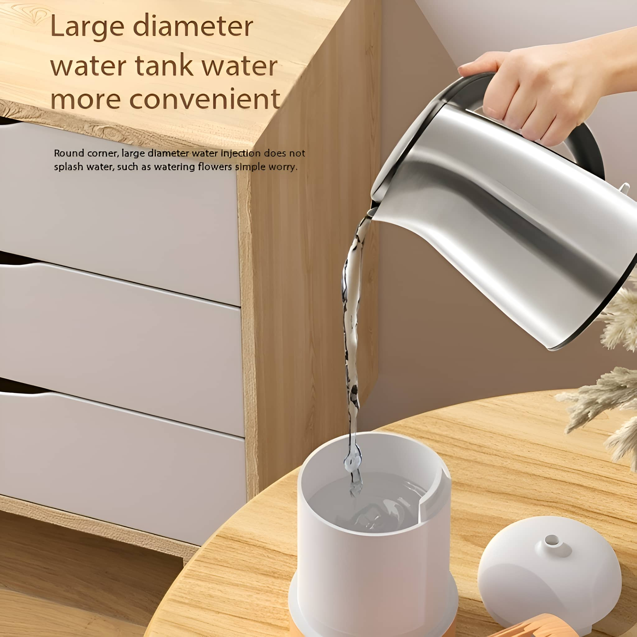 Eine Hand gießt Wasser aus einem silbernen Wasserkocher in einen weißen Behälter. Holztisch und weiße Schubladen.