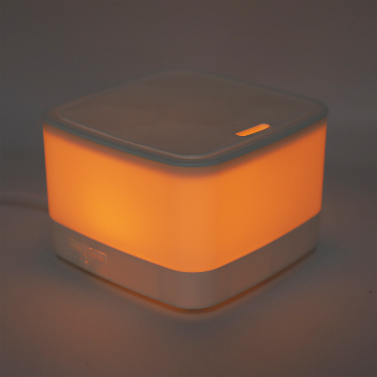 Ein kleiner, weißer, quadratischer Diffusor für ätherische Öle, der orangefarben leuchtet.
