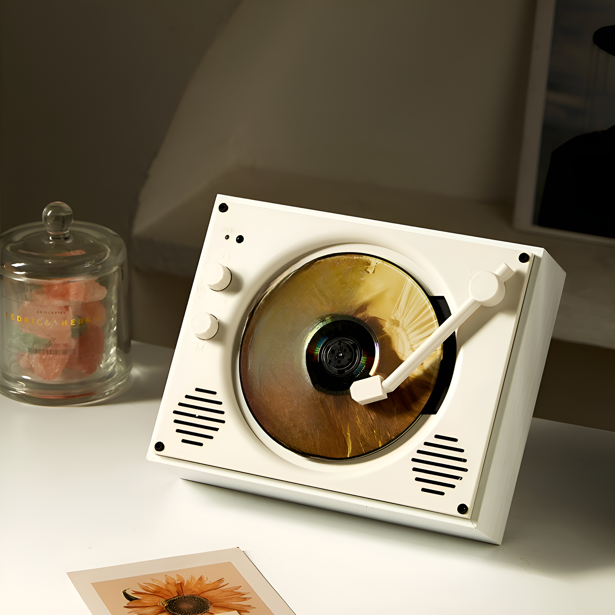 Ein weißer Plattenspieler mit CD, neben einem Glas und einem Bild.