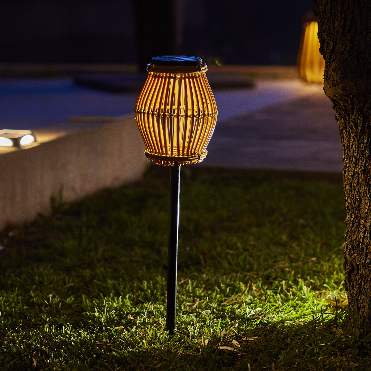 Eine beleuchtete Solar-Laterne im Garten bei Nacht, mit Grasvordergrund und dunklem Hintergrund.