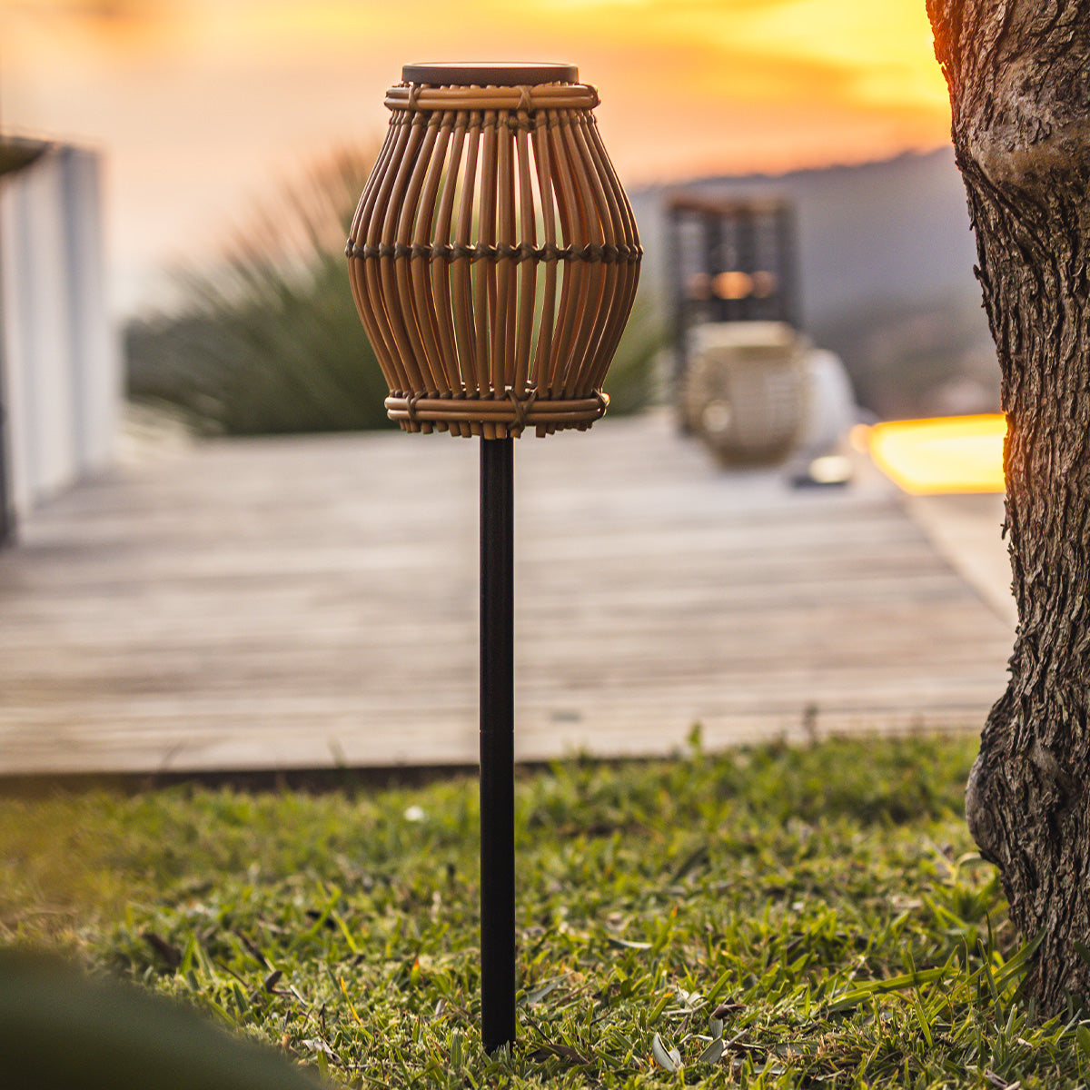 Solar-Lampe im Bambus-Stil auf grünem Rasen, Sonnenuntergang im Hintergrund.
