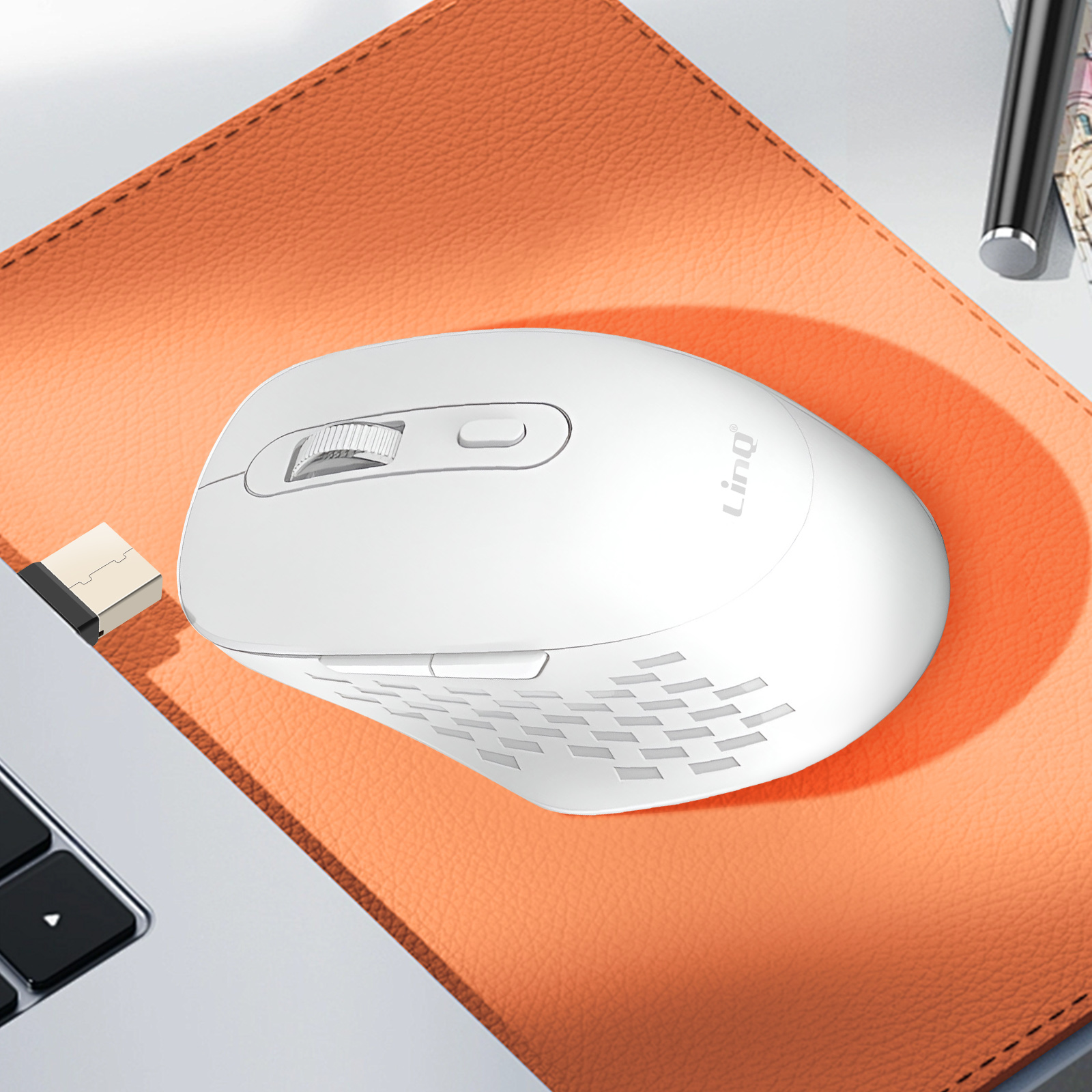 Eine weiße, kabellose Maus auf einem orangefarbenen, strukturierten Mauspads. Ein Laptop im Hintergrund.