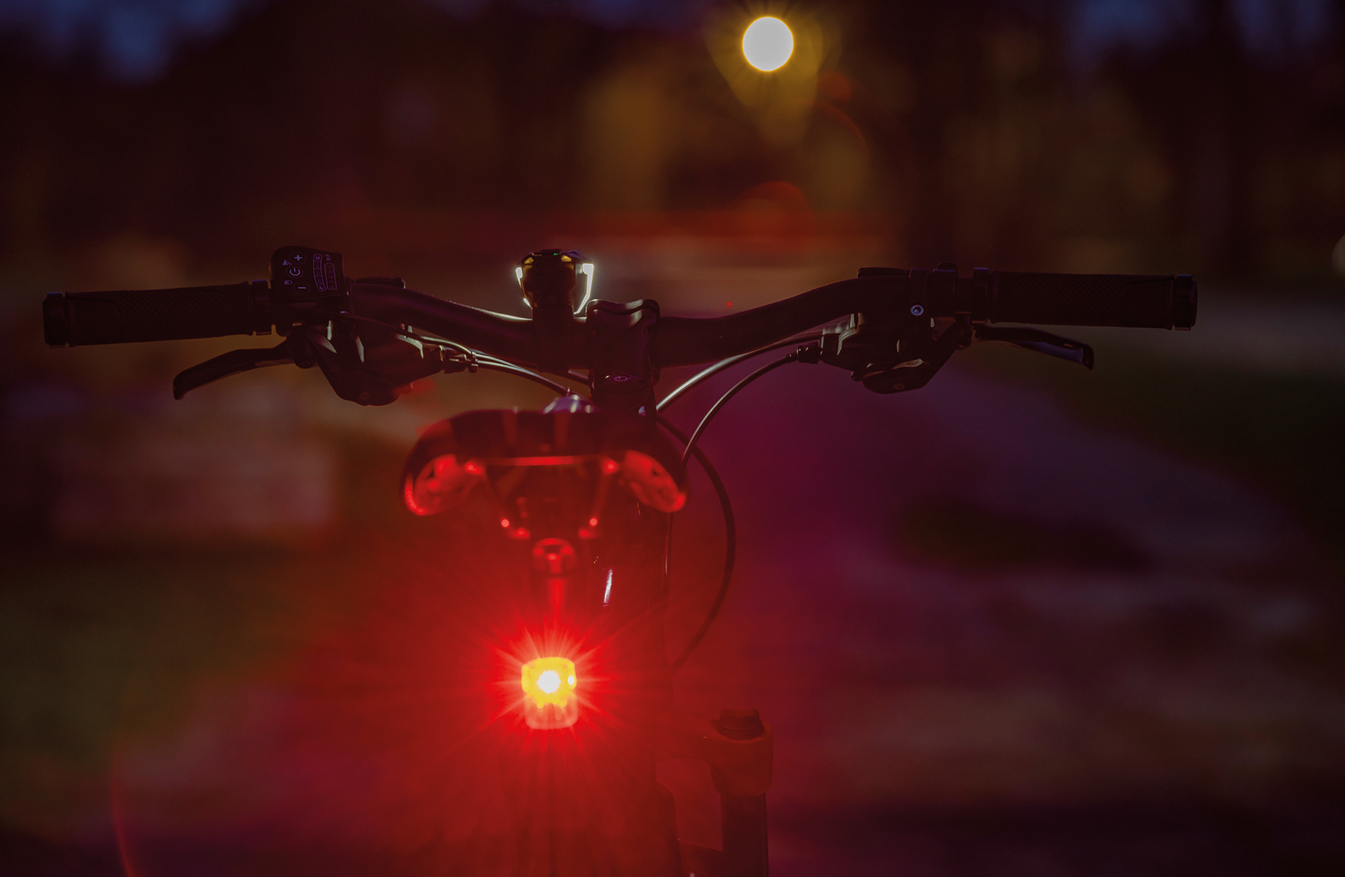 Fahrradlenker mit rotem Rücklicht. Nachtszene mit verschwommenen Lichtern.