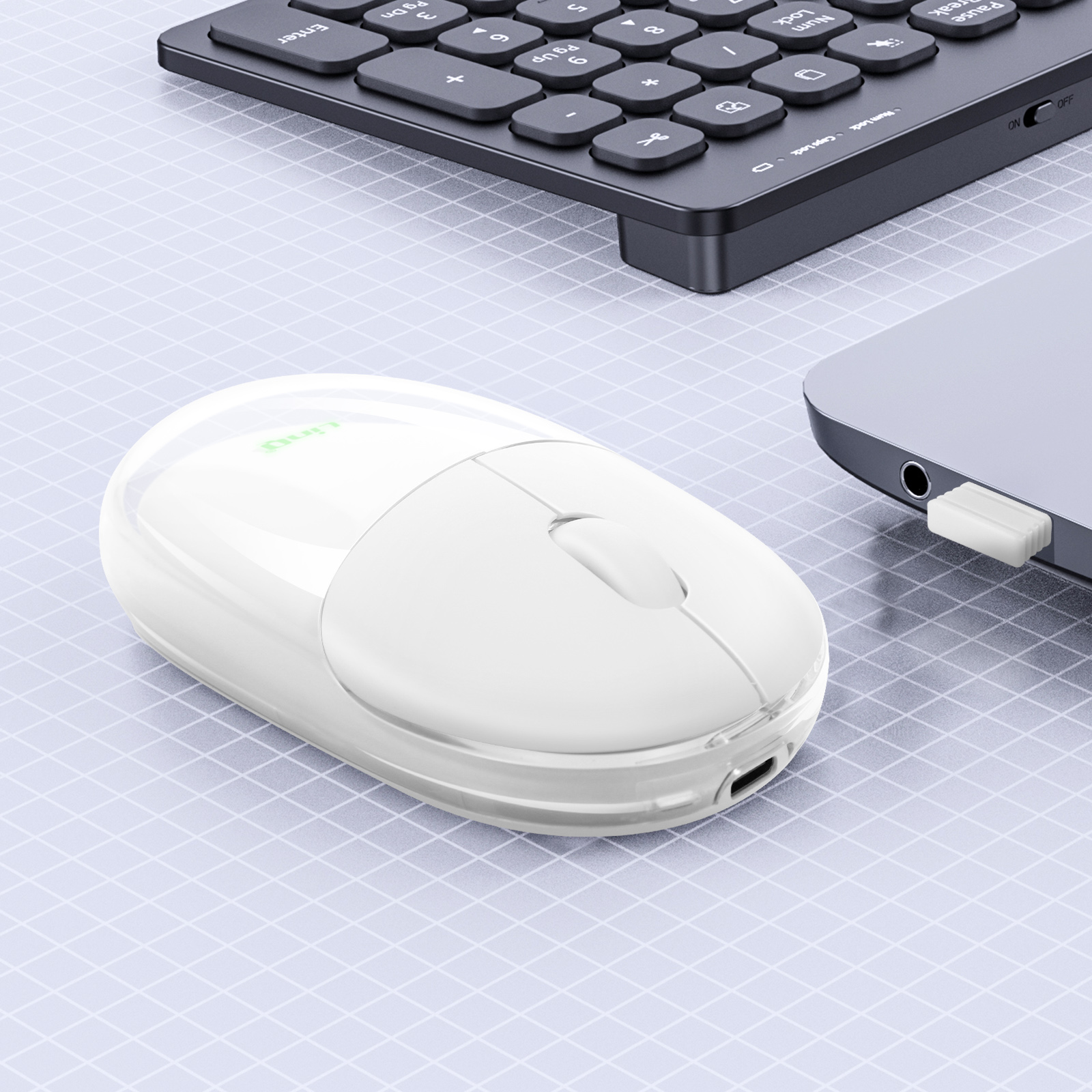 Eine weiße, kabellose Maus mit Ladeanschluss neben Laptop und Tastatur.