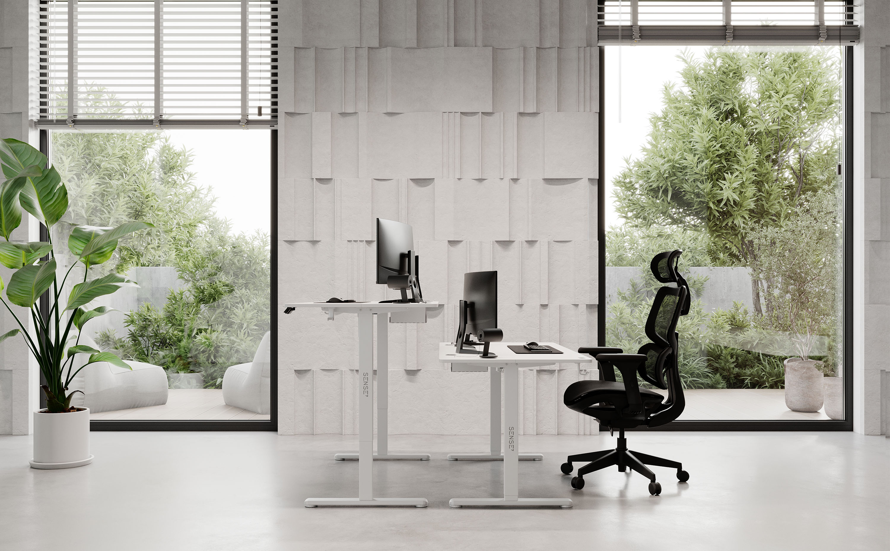 Büro mit zwei weißen Schreibtischen, Monitoren und einem schwarzen Stuhl. Fenster blicken auf einen Garten.
