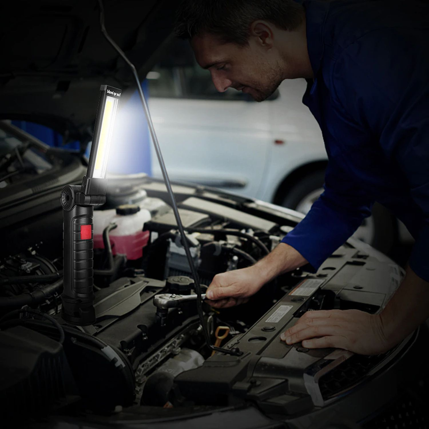 Ein Mann arbeitet mit einer Arbeitsleuchte an einem Automotor. Die Motorhaube ist offen und der Motor sichtbar.