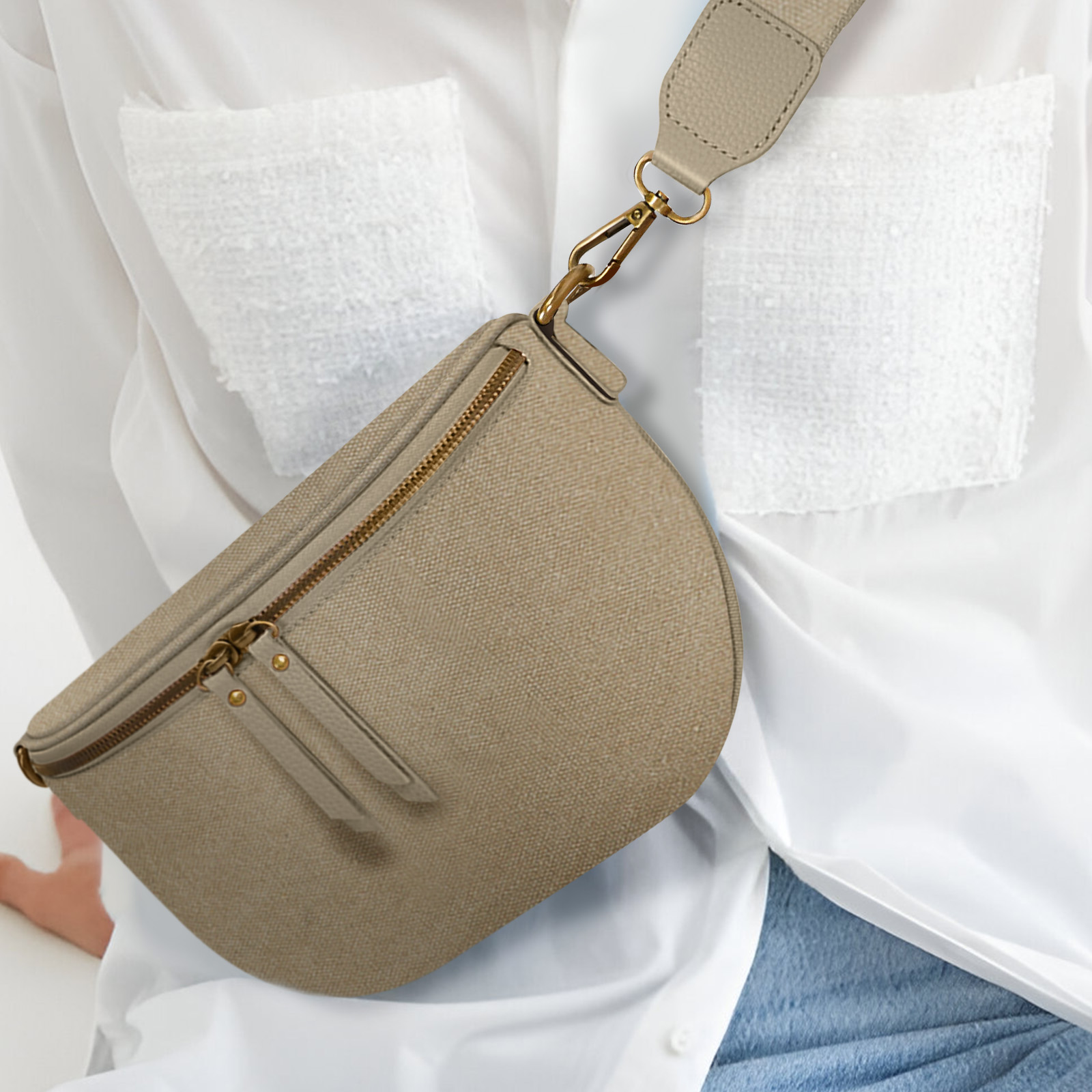 Un bolso en forma de media luna, de color beige claro, con una correa larga, sobre una camisa blanca.