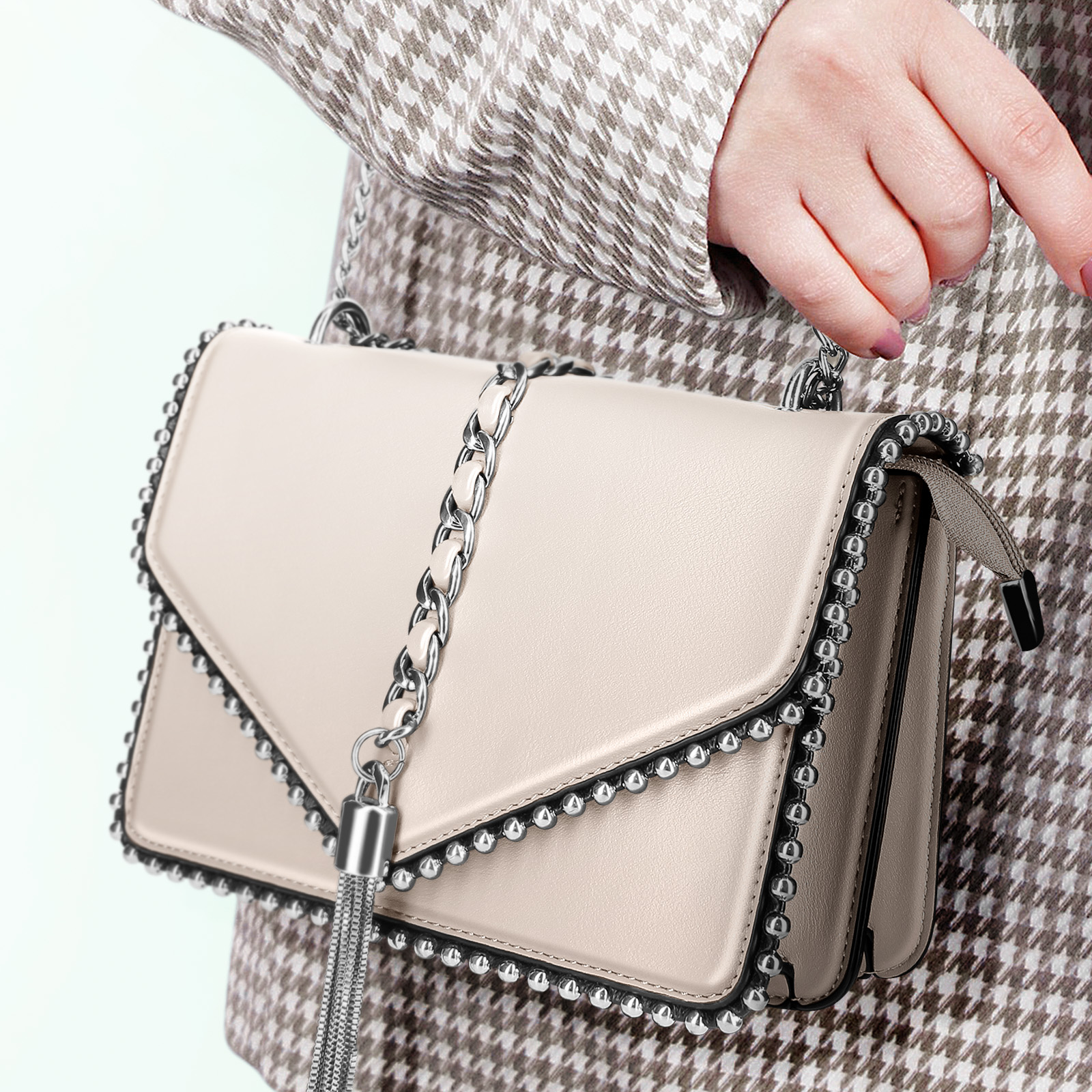 Die Hand einer Frau hält eine cremefarbene Handtasche mit silbernen Nieten und einer Kette.