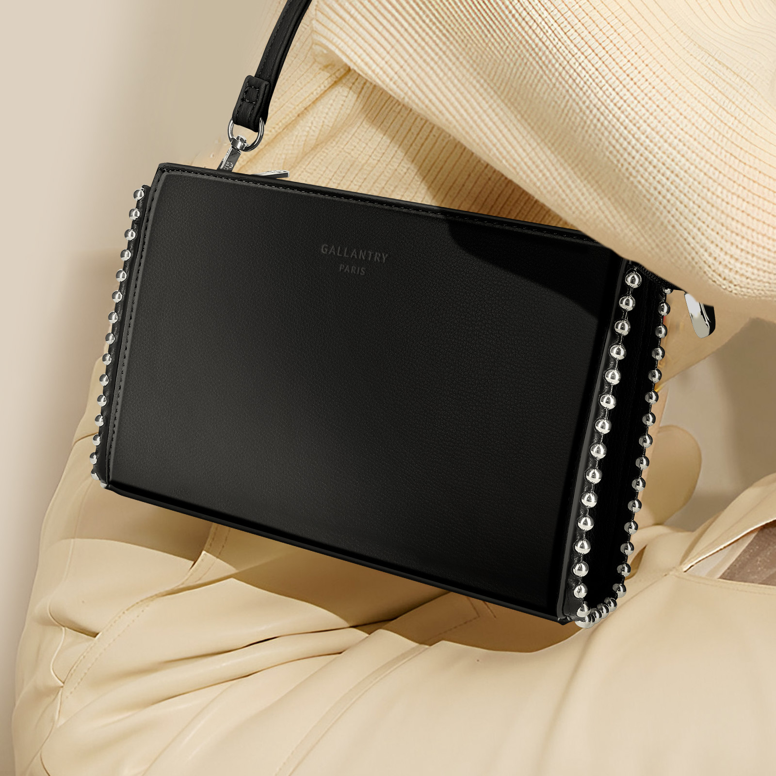 Schwarze Handtasche mit silbernen Nieten an den Rändern. Die Tasche wird von einer Person gehalten.