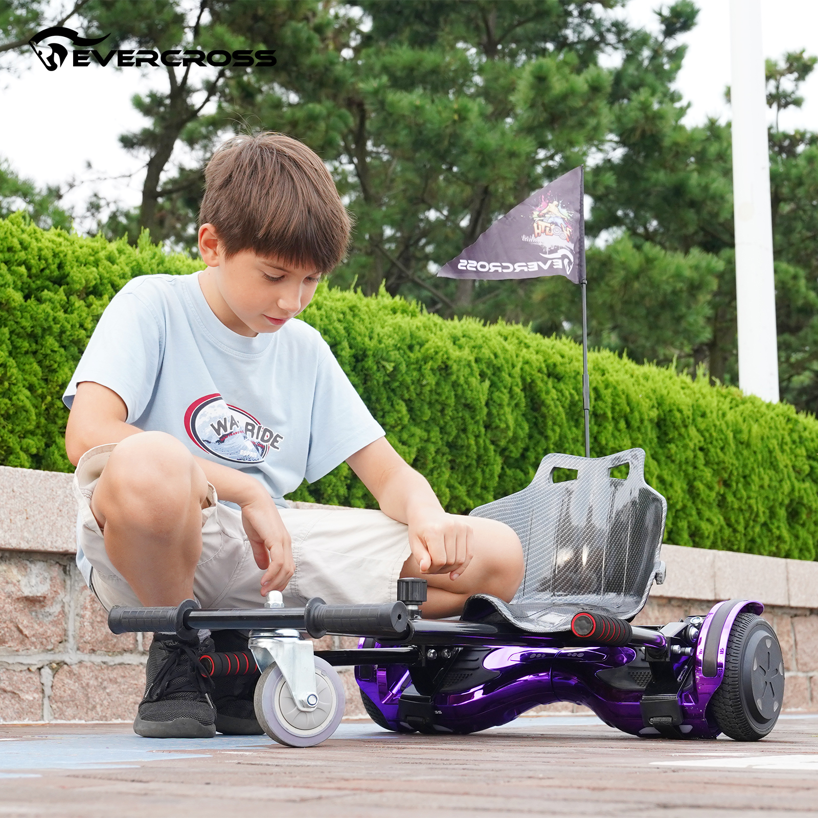Ein Junge sitzt auf einem lila Hoverboard mit Rädern und blickt nach unten. Grüne Büsche und eine Flagge dahinter.